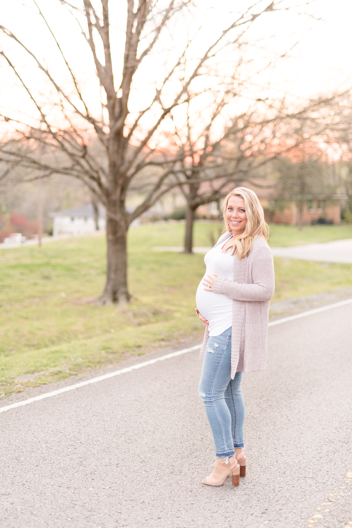 Expecting mother holds bump and smiles.