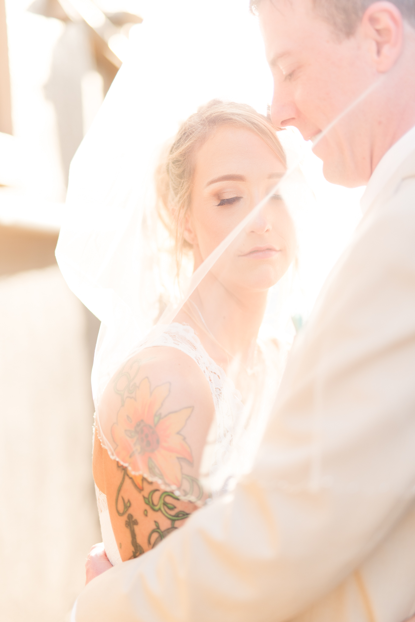 Bride and groom hug under veil at sunset.