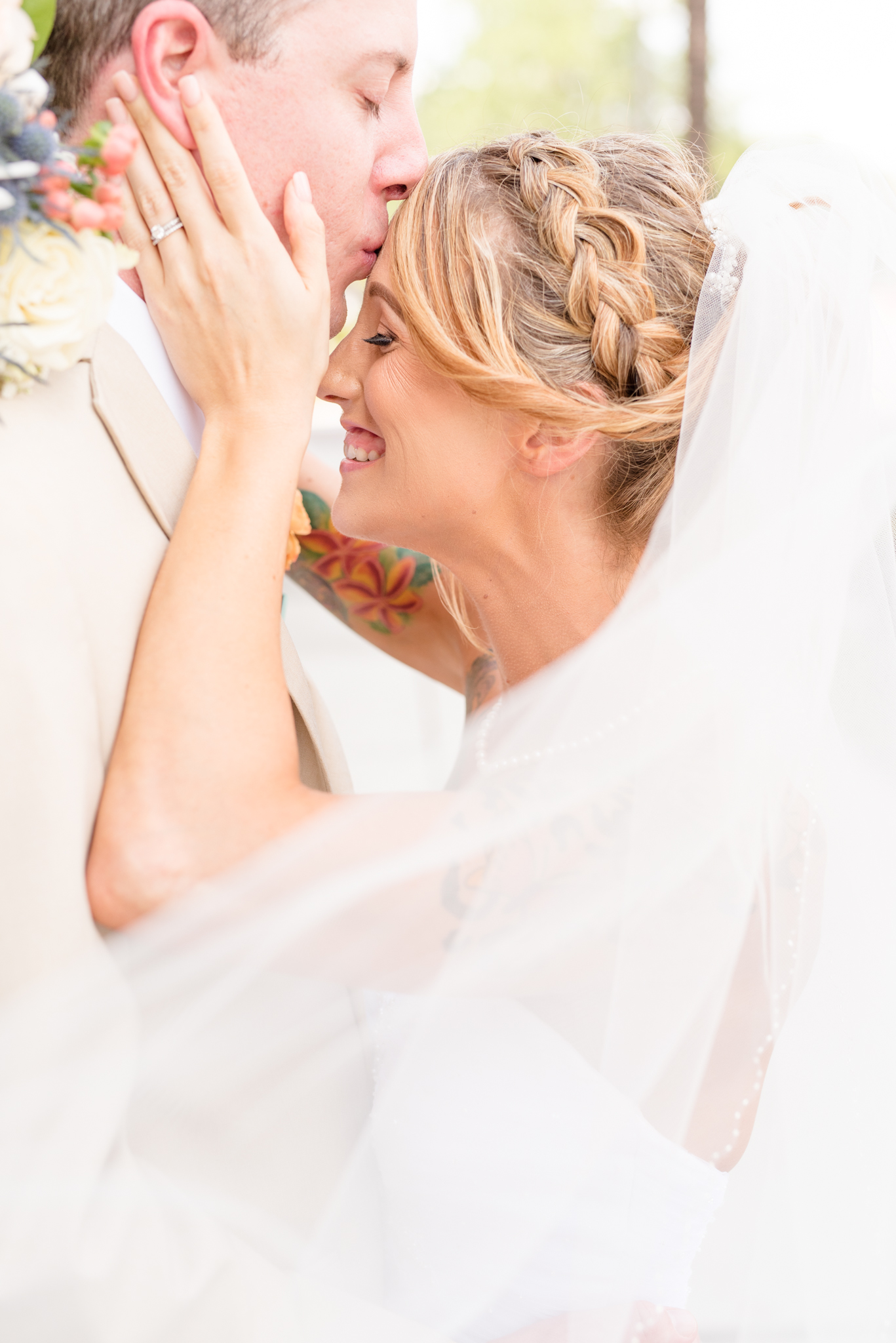 Groom kisses brides forehead while she smiles.