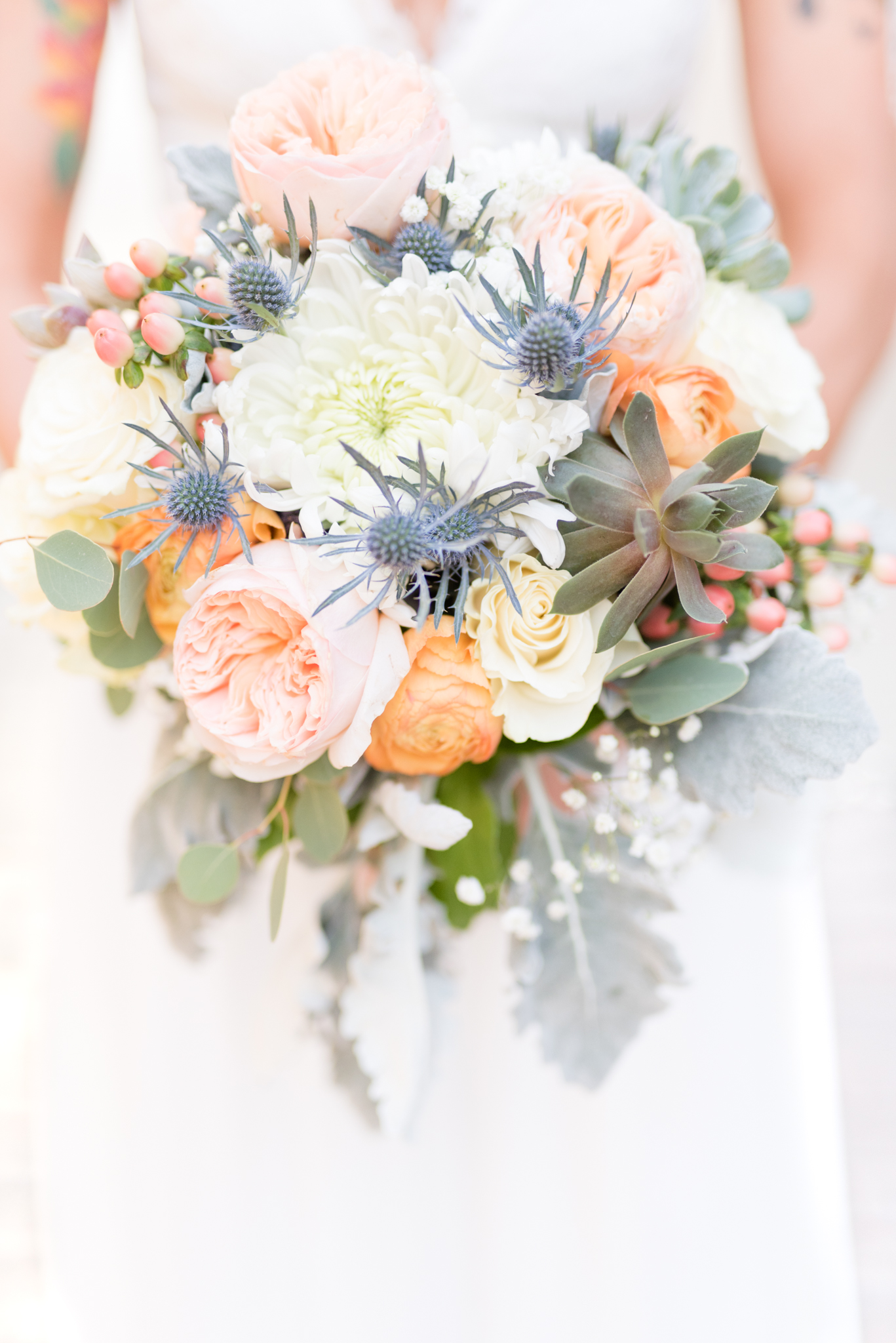 Bride holds bouquet on peonies and succulents.