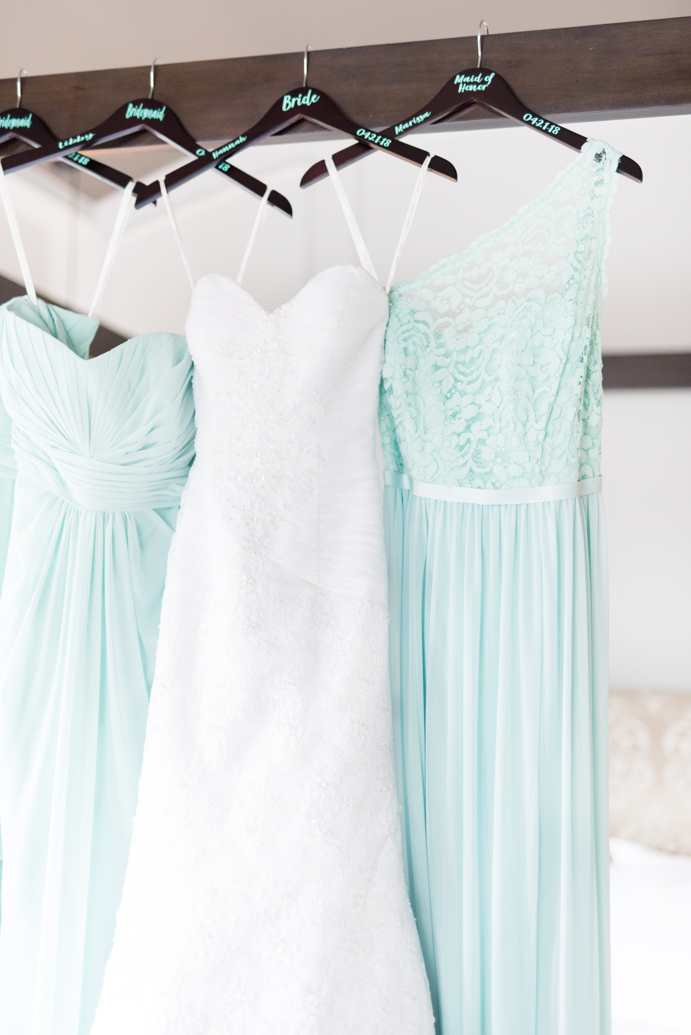 Bride and bridesmaid dresses hand on bed.