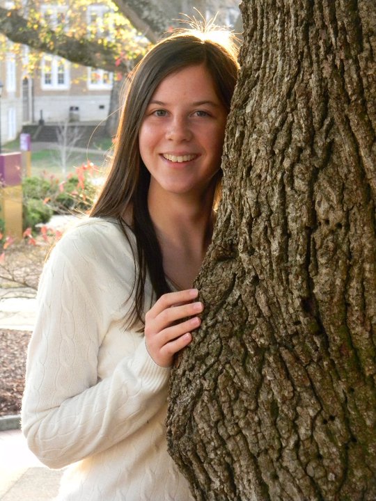 Girl leans against a tree and smiles.