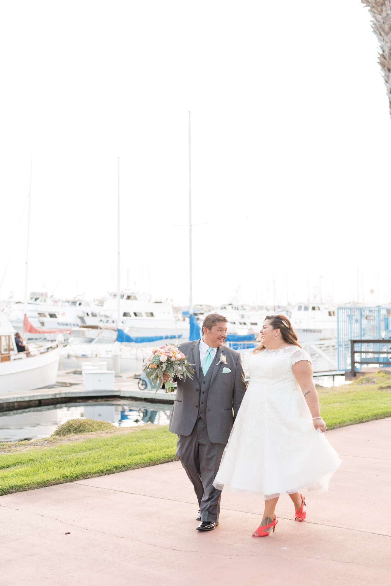 Bride and groom walk along marina.