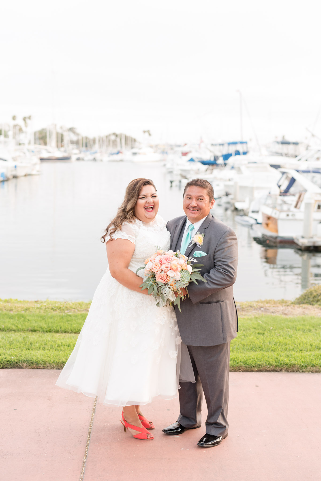 Bride and groom laugh while in front of a marina.
