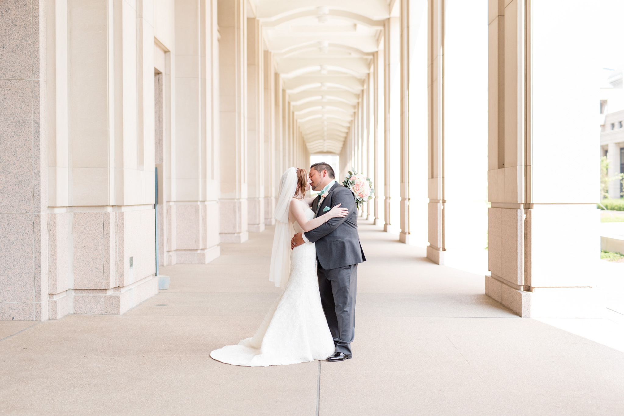 Bride and groom kiss among pillars.