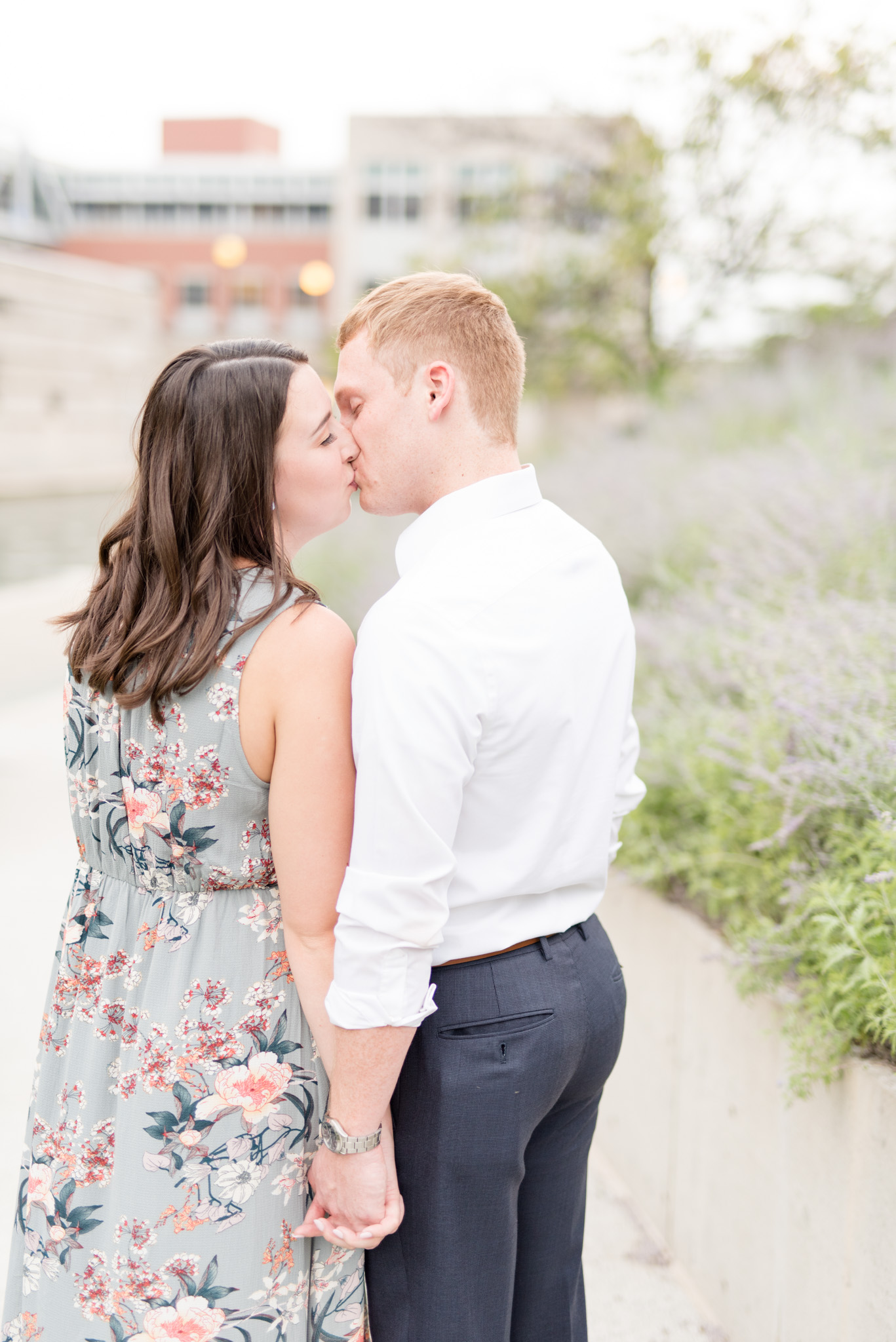 Engaged couple kisses while holding hands.