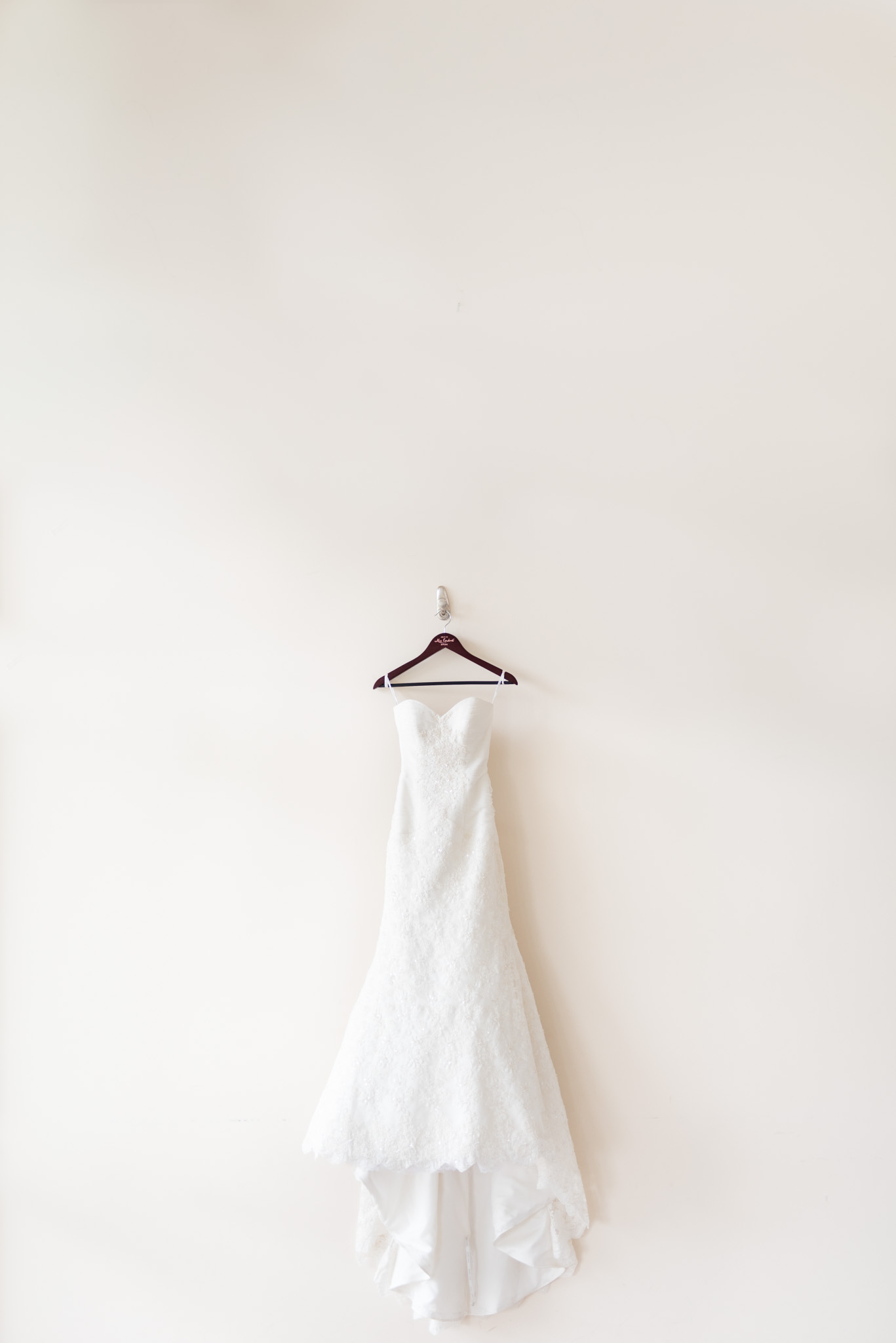 Wedding dress hangs on large cream wall.