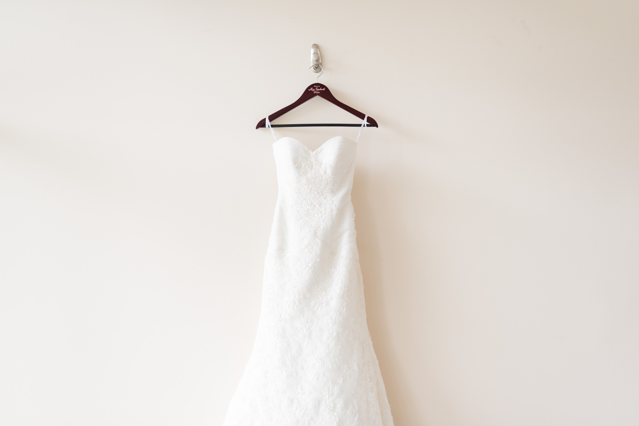 Brides dress hangs on cream wall.