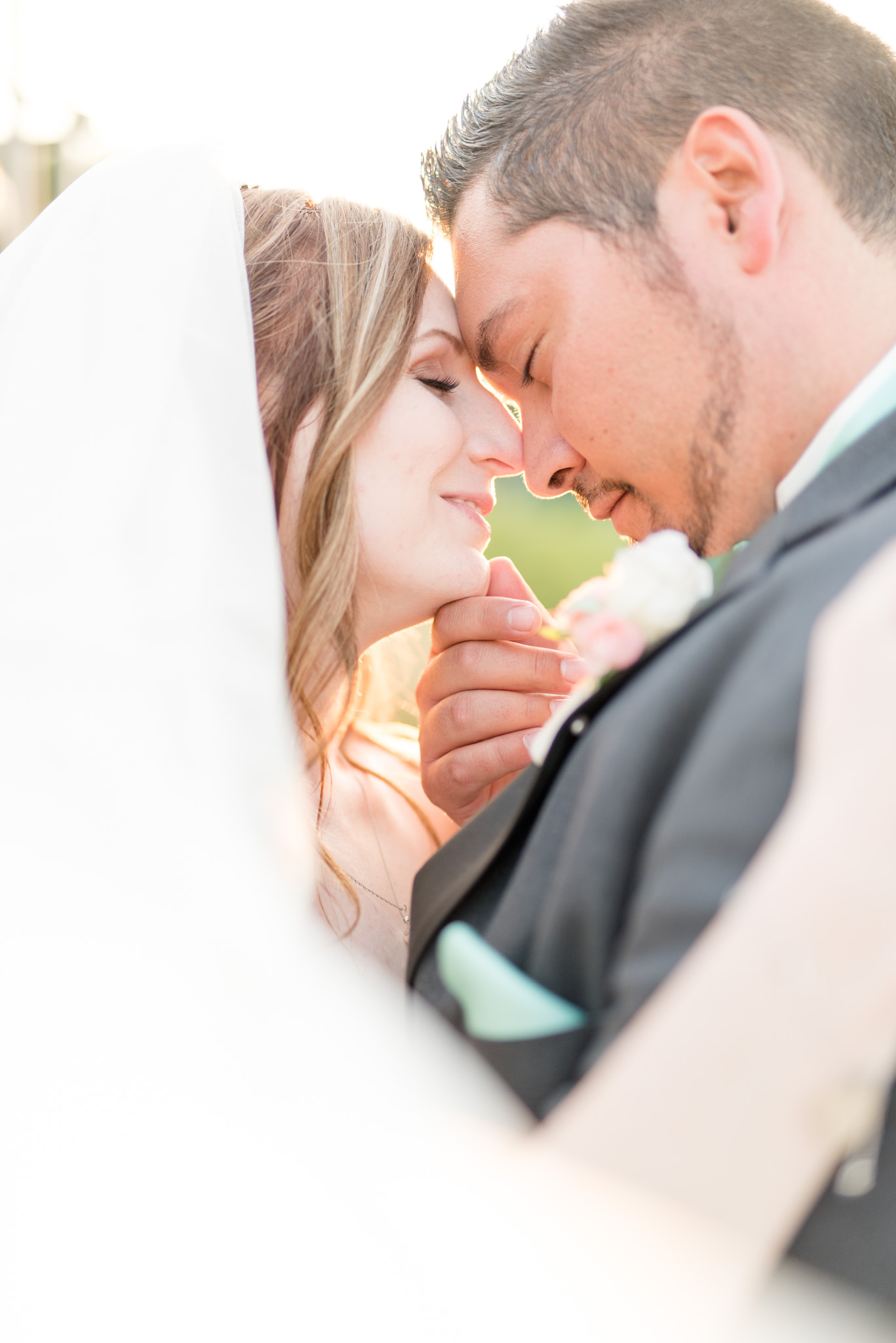 Bride and groom nuzzle together at sunset.