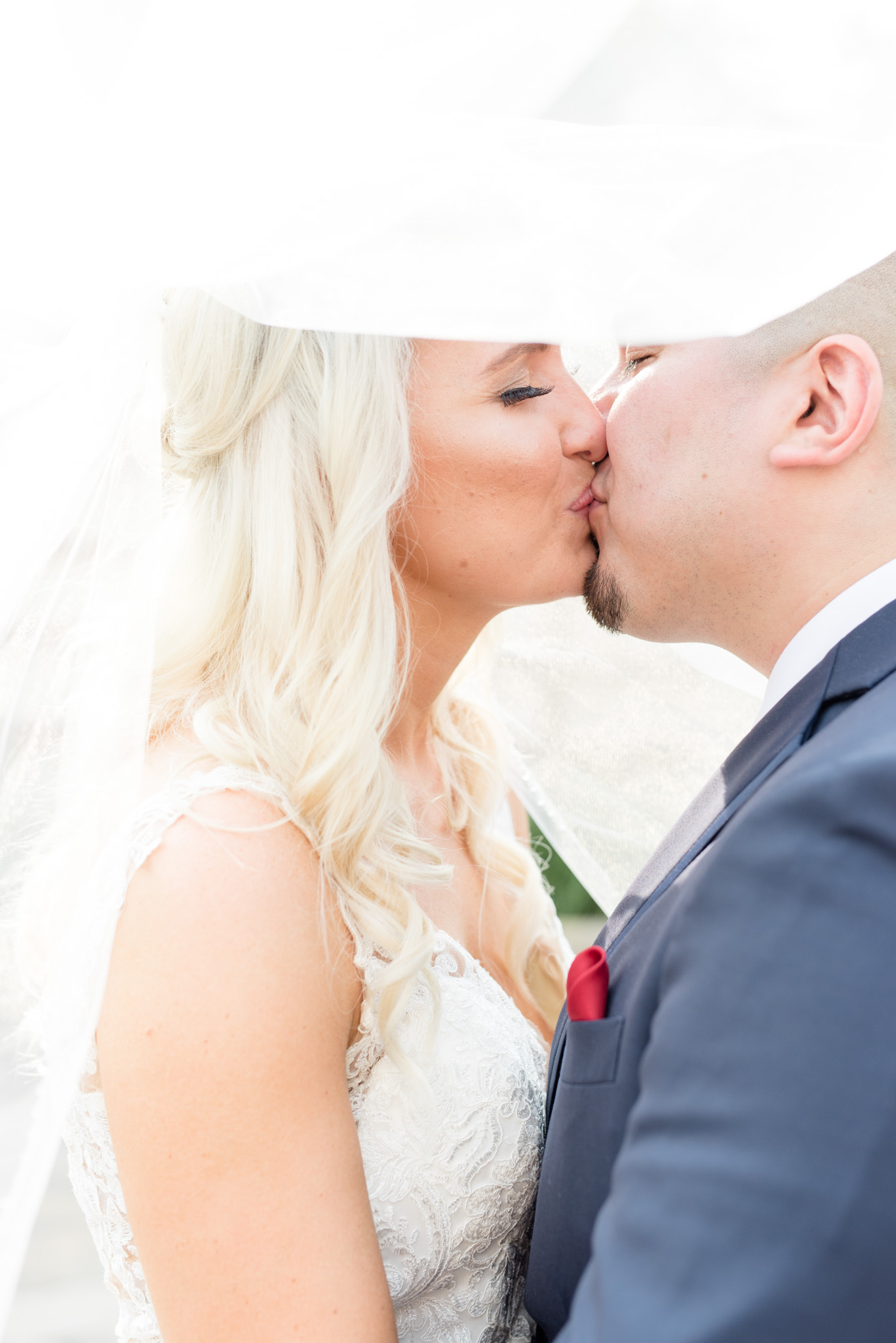 Bride and groom kiss under veil. 