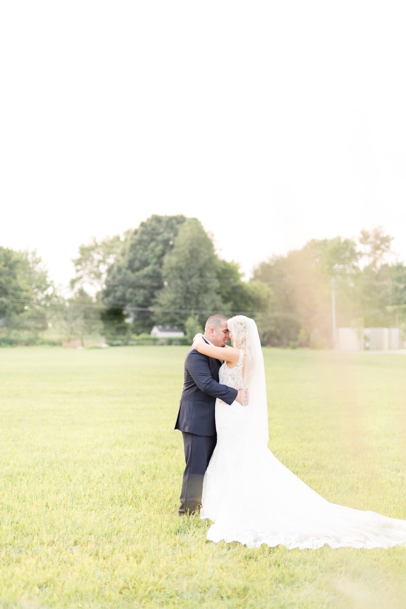 Bride and groom snuggle in field.