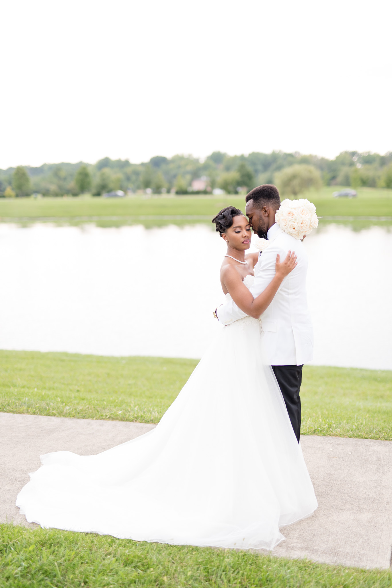 Bride and groom hug next to lake.