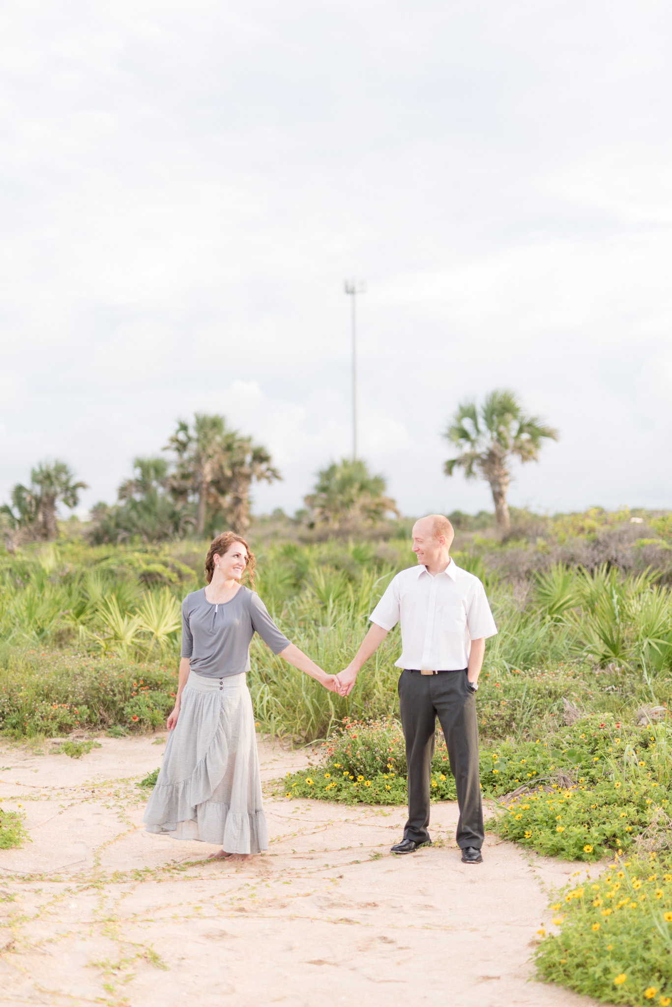 Couple holds hands in front of palm trees.