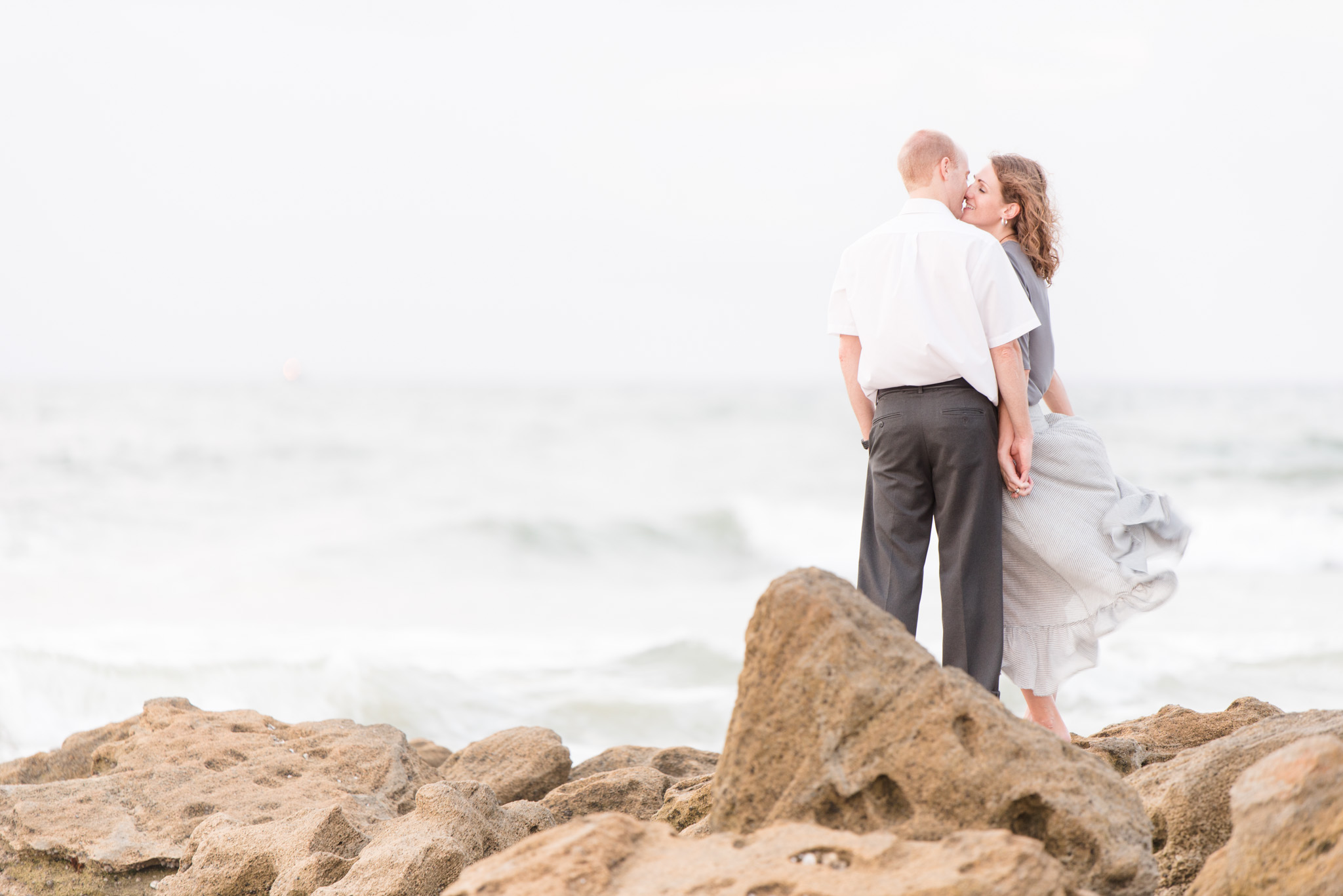 Couple kisses on beach rocks.