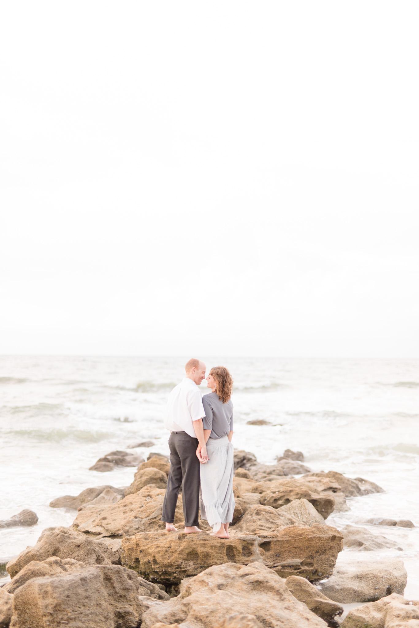 Couple stands on beach rocks.