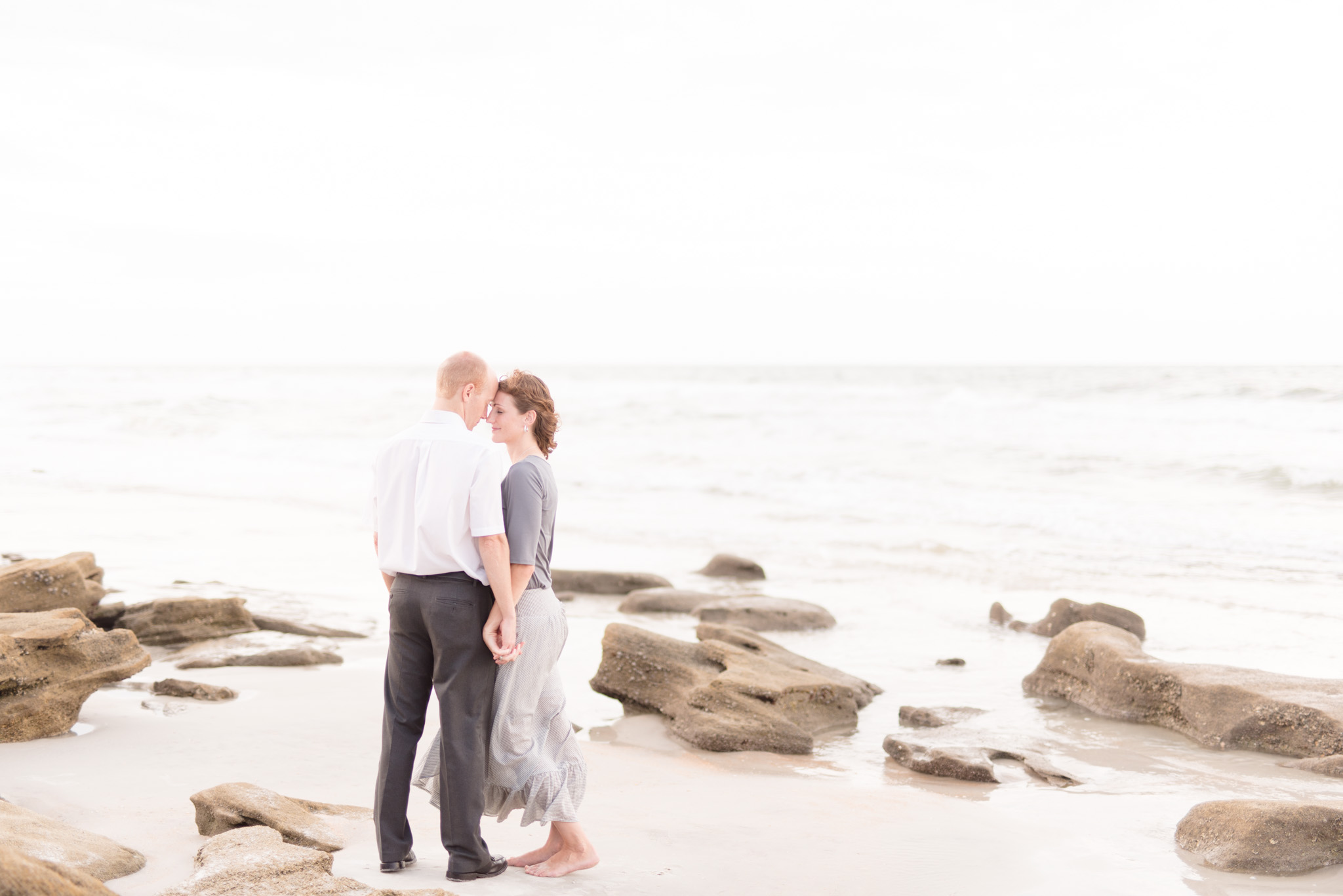 Couple holds hands by beach rocks.