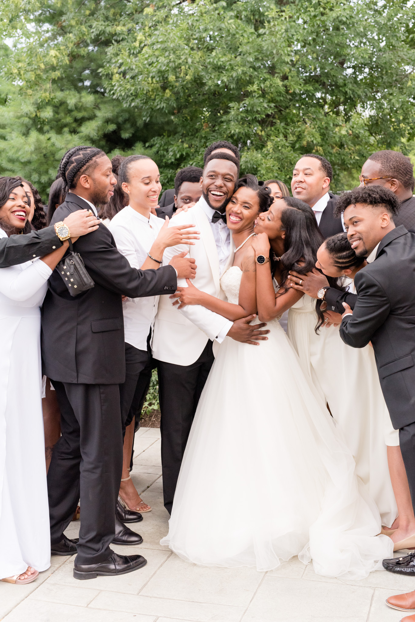 Wedding party hugs bride and groom.