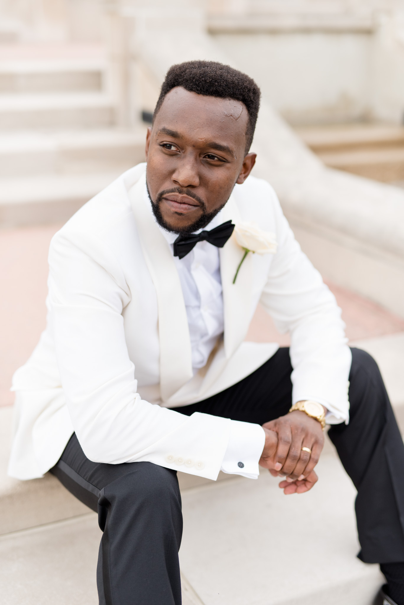 Groom sits on steps and looks over shoulder.