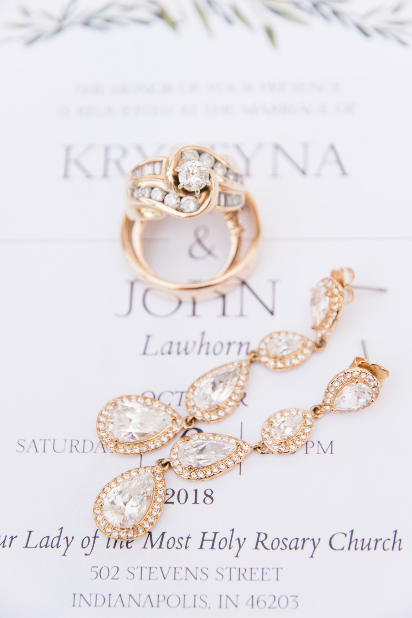 Wedding rings and earrings sit on invitation