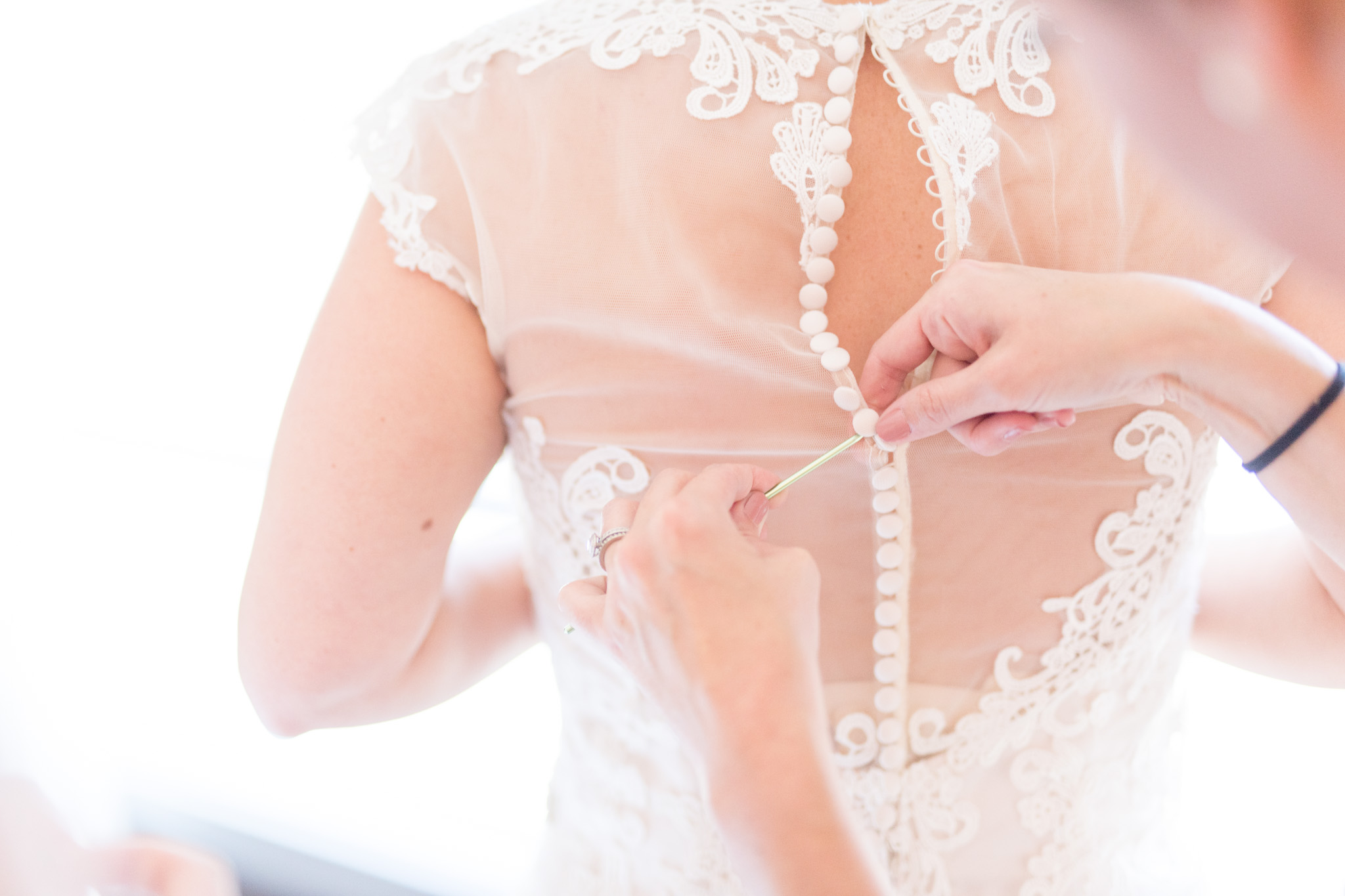 Bridesmaids help bride button wedding dress.