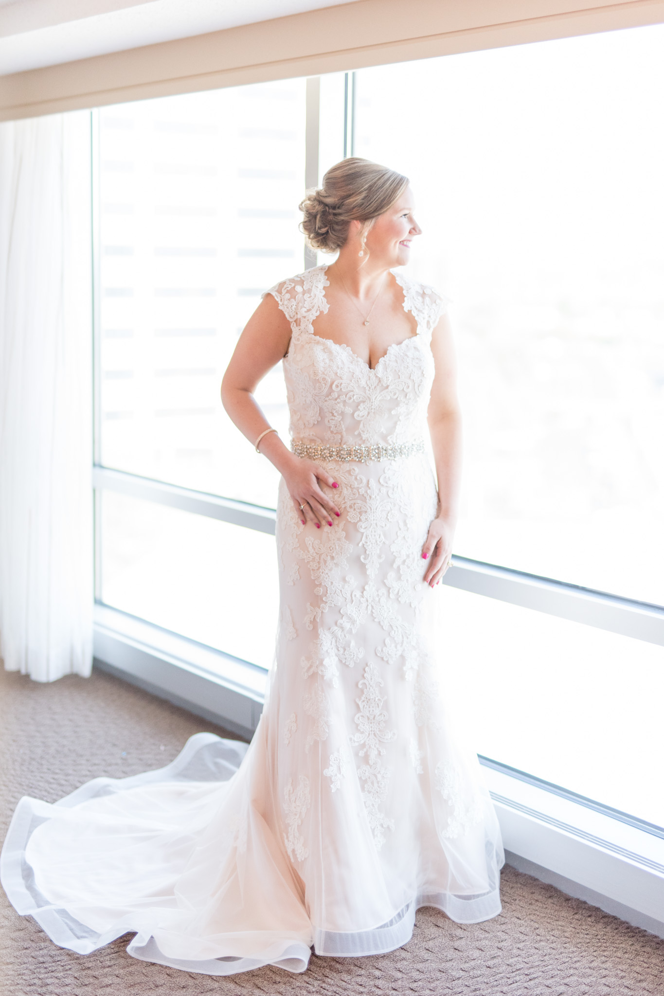 Bride looks out hotel room window.