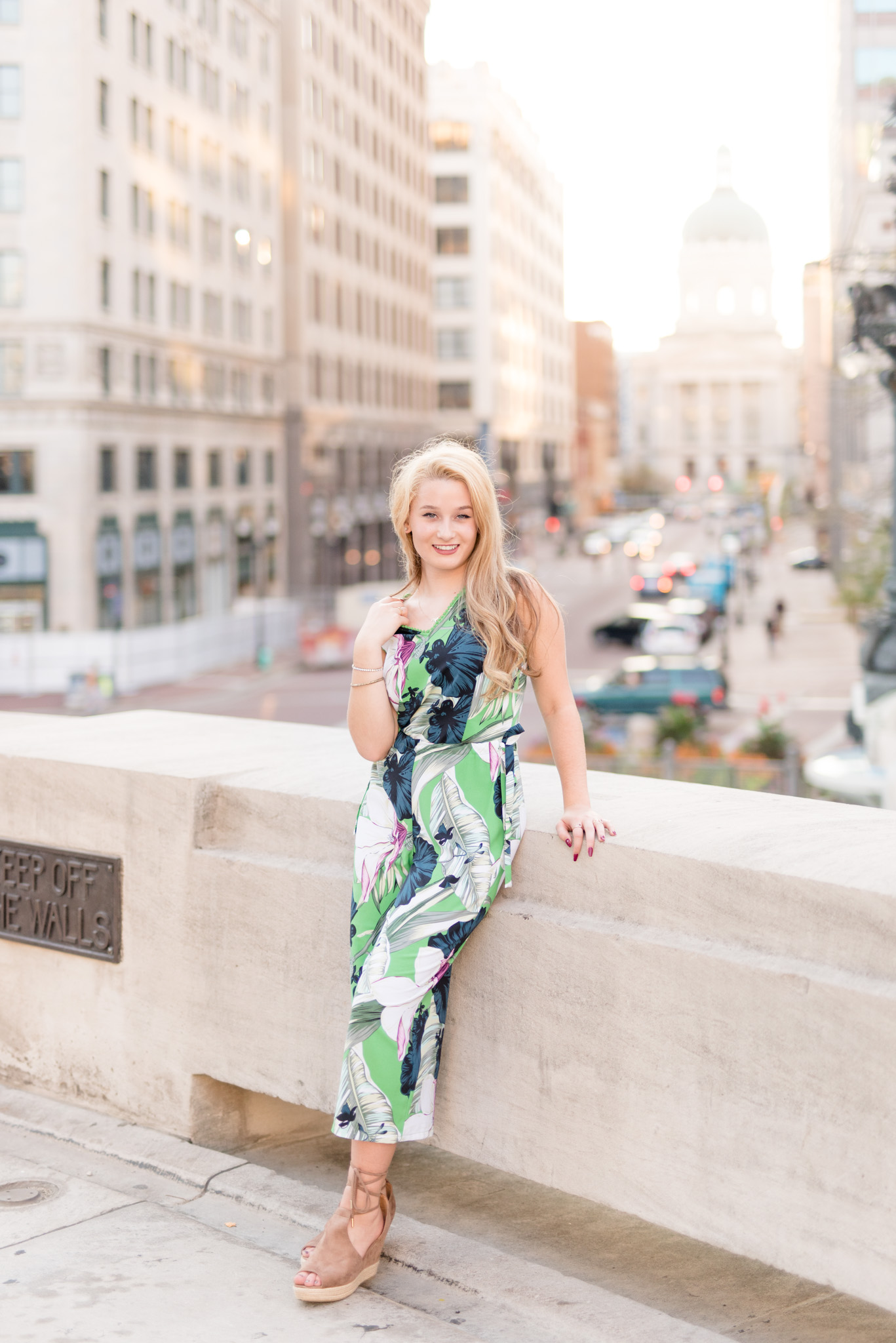 Senior leans against wall in downtown Indianapolis at sunset.