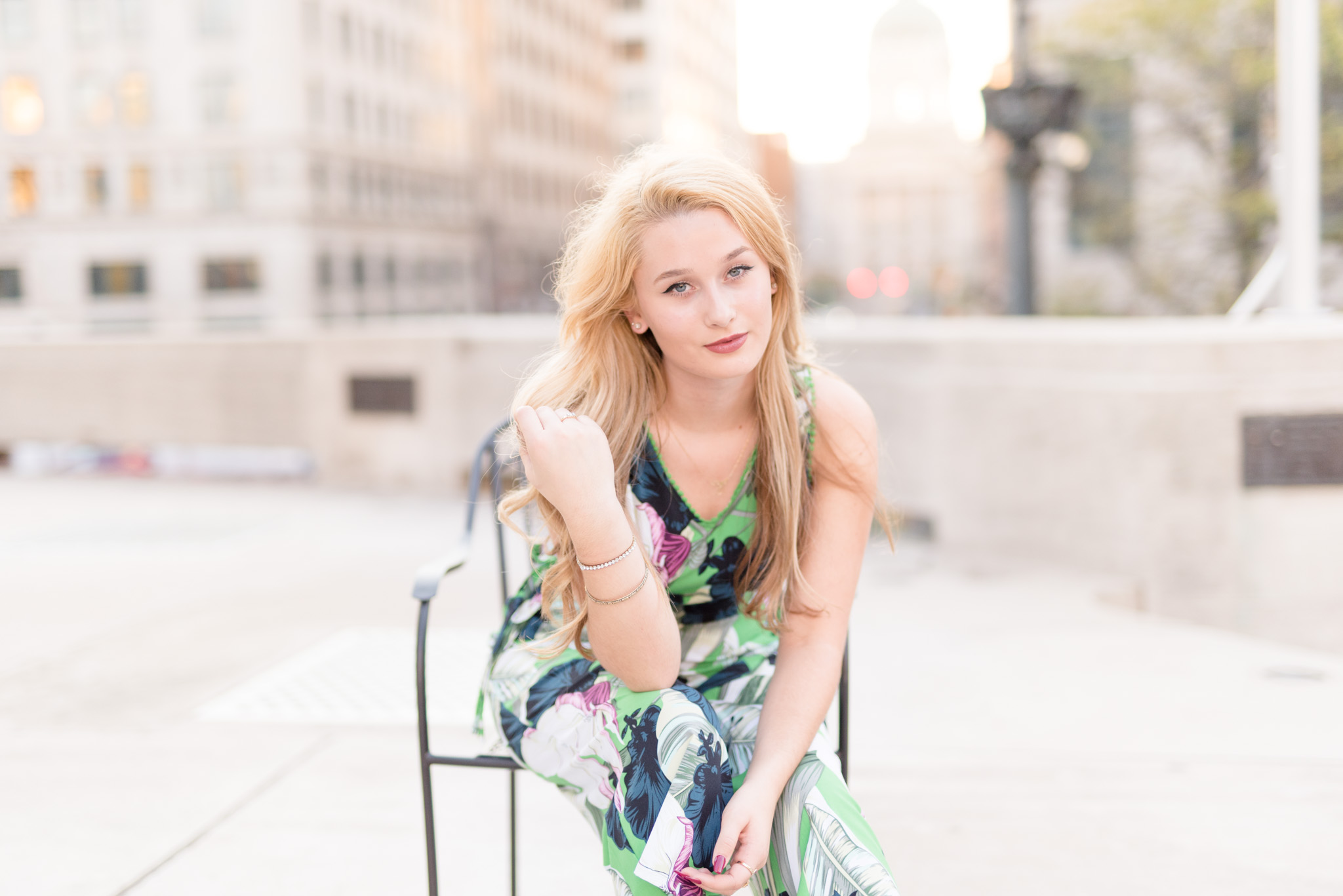 Senior girl sits and leans forward at sunset.