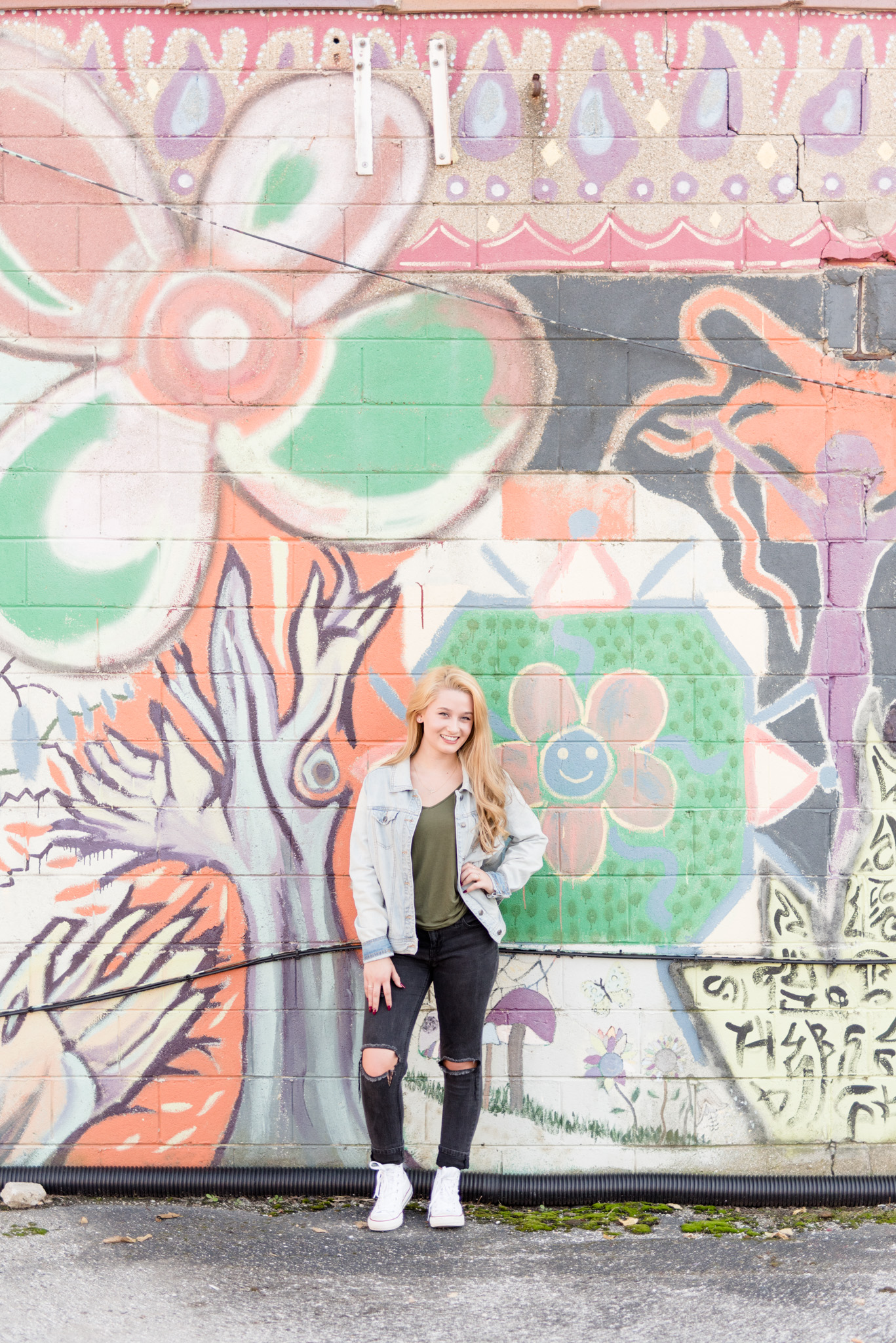 Senior girl stands in front of painted wall.