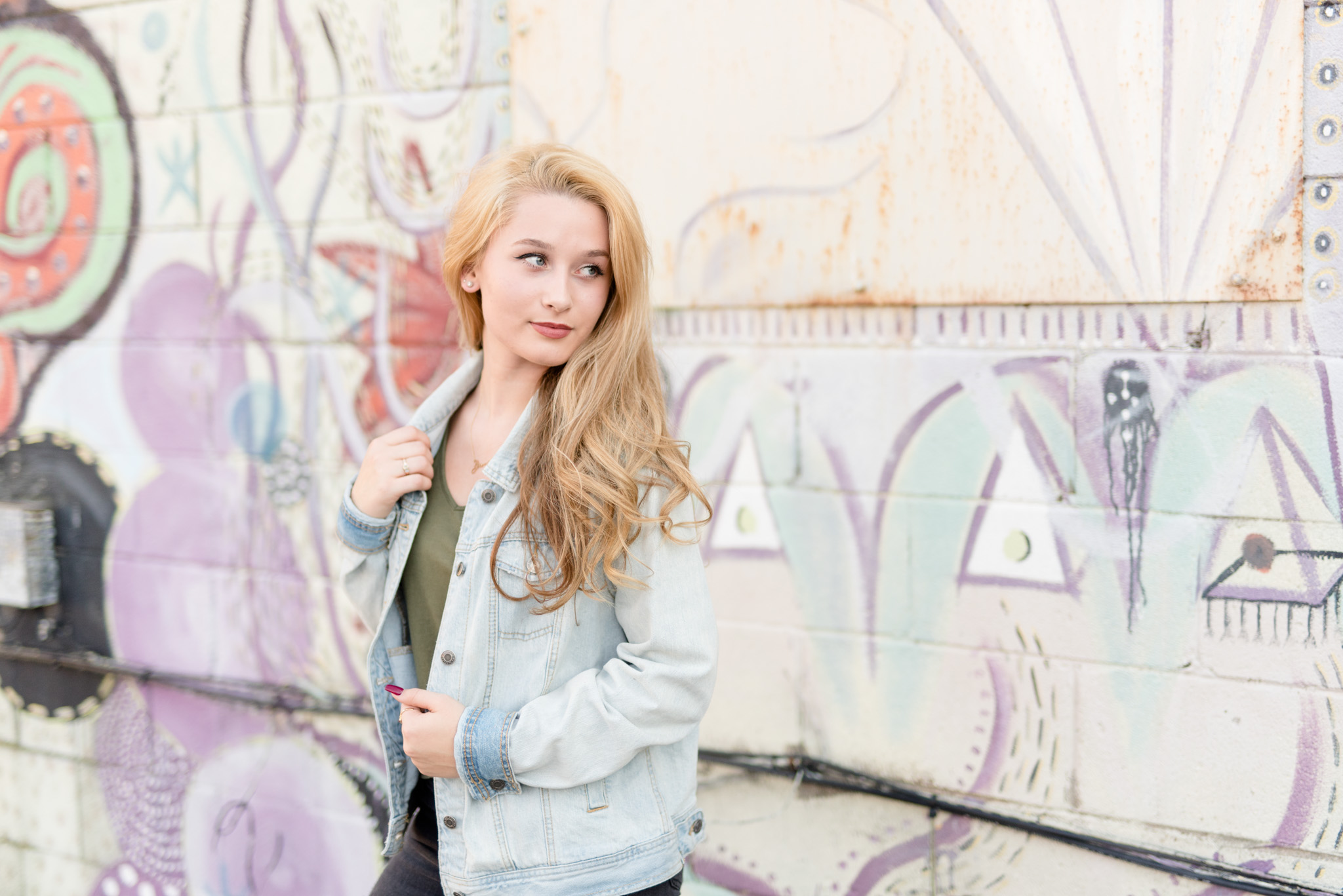 Senior girl looks to side in front of fountain square painted wall.