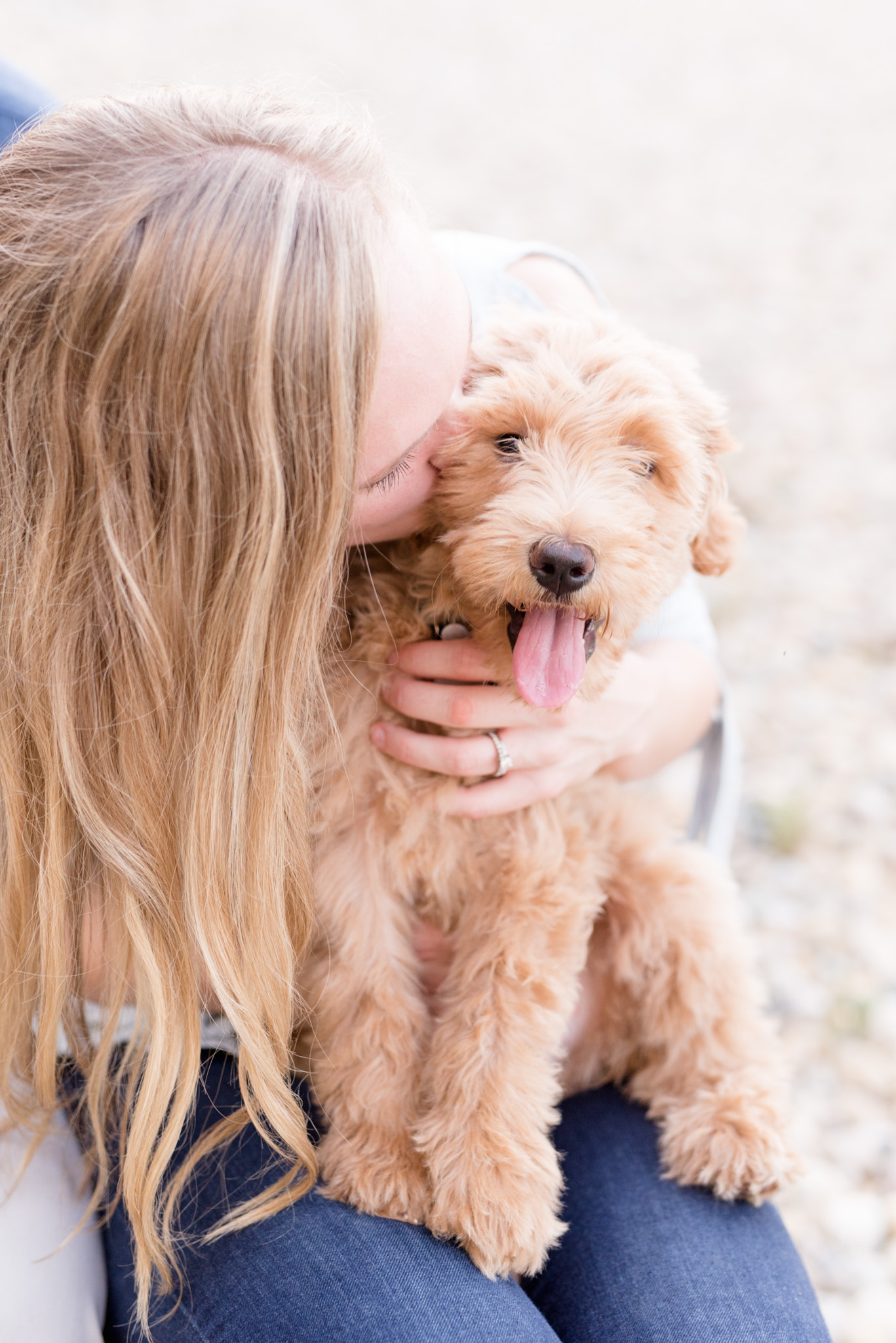 Woman kisses golden doodle puppy.