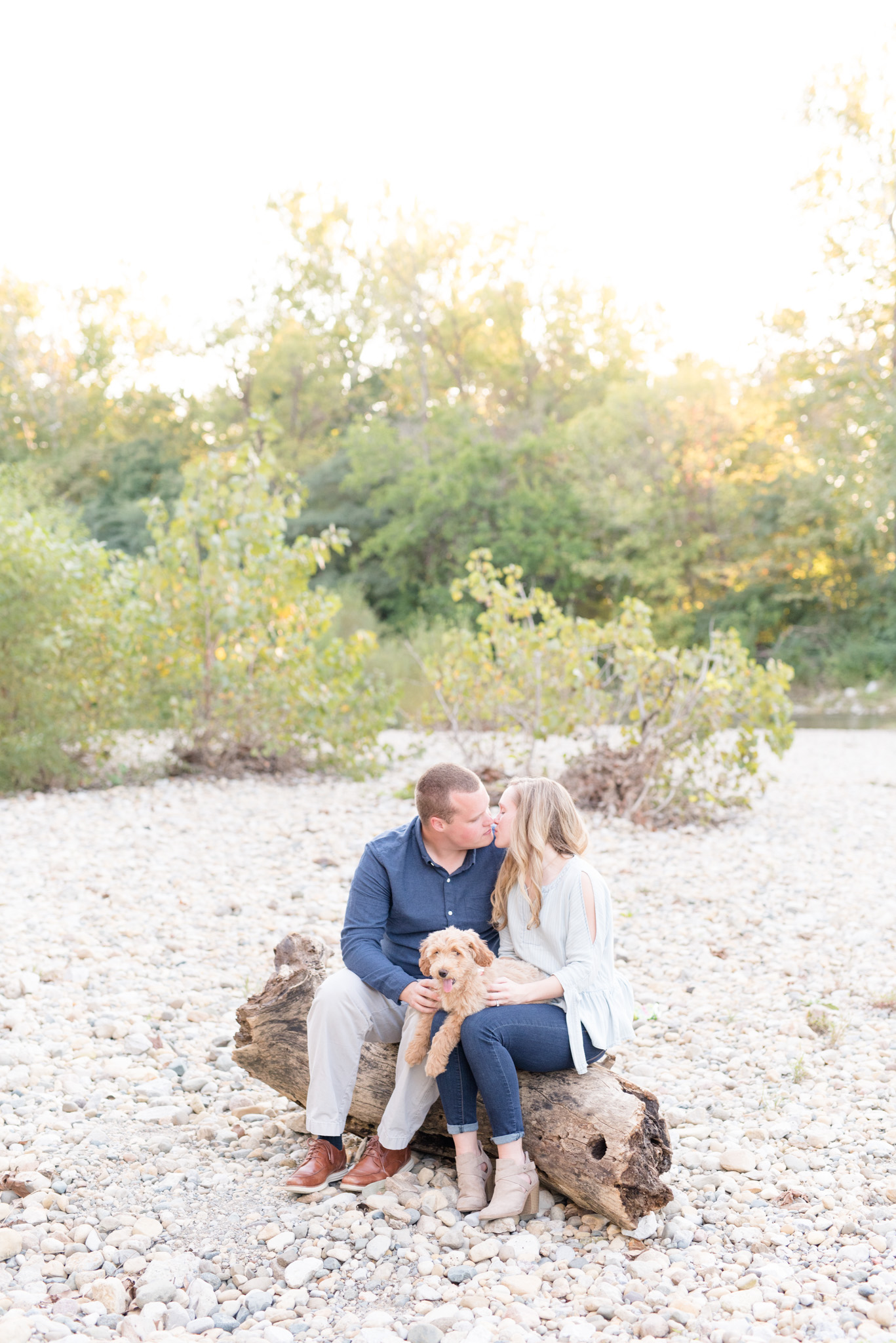 Couple kisses while holding goldendoodle puppy.