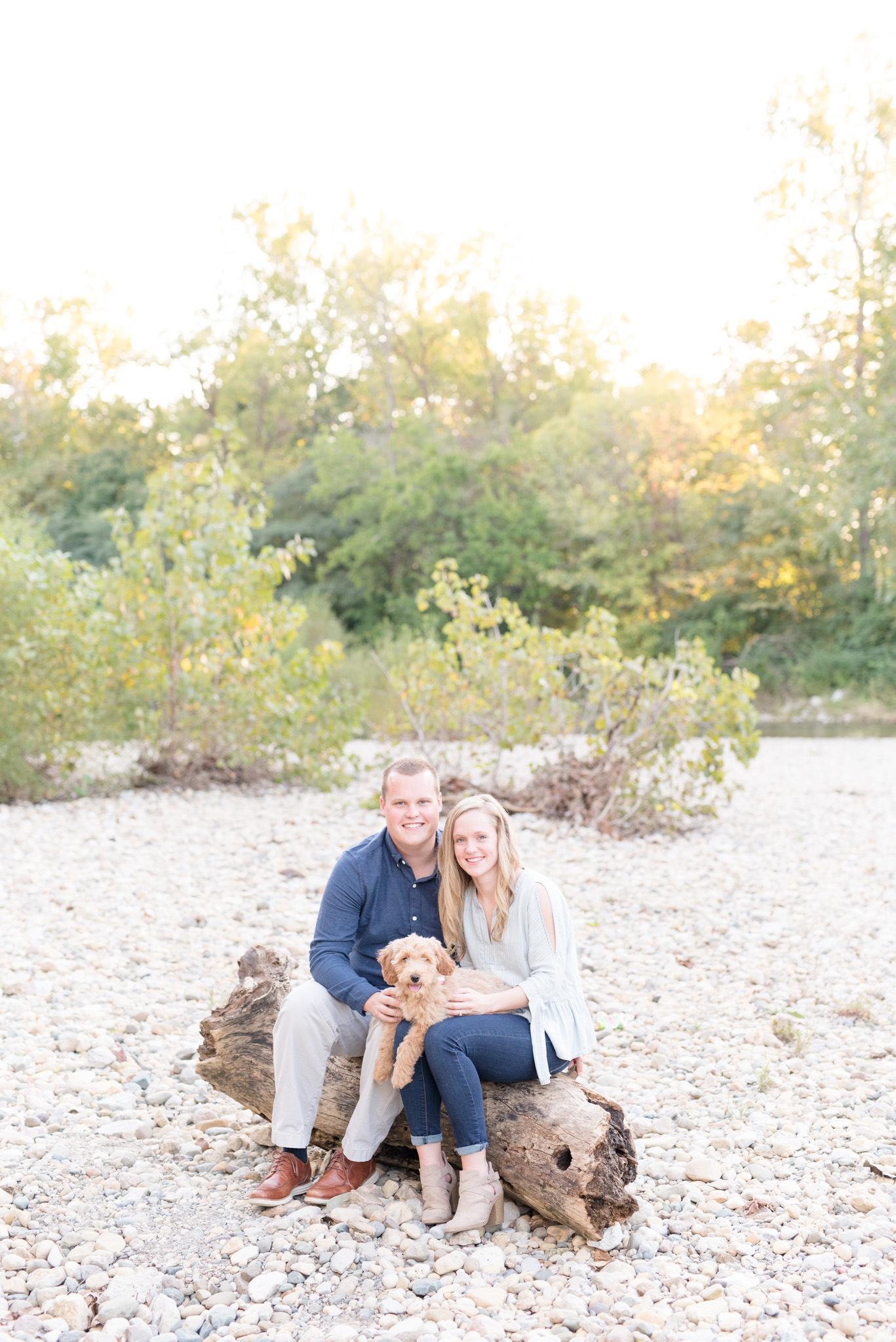 Couple sits on log with puppy in lap.