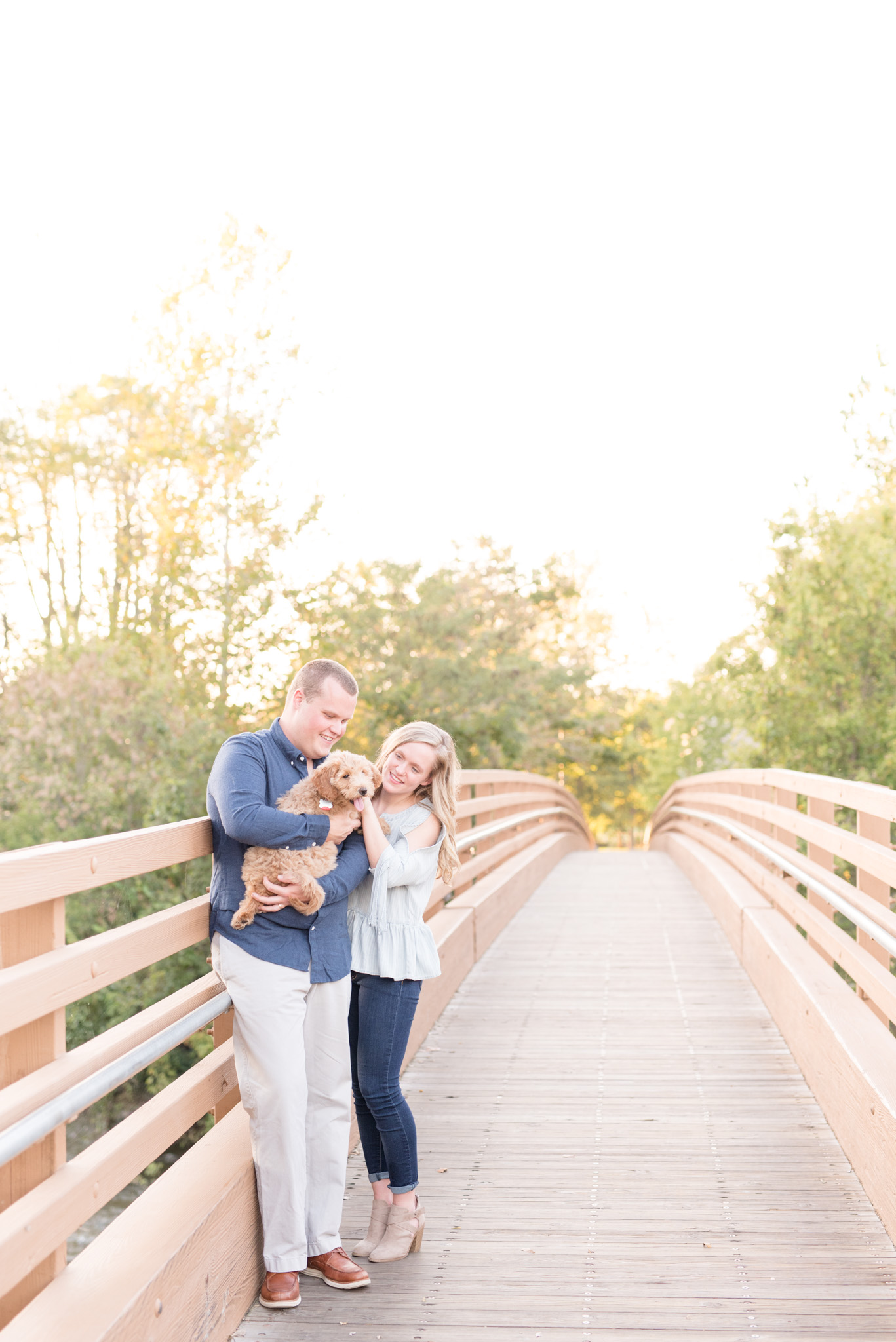 Couple cuddles on bridge with goldendoodle puppy.