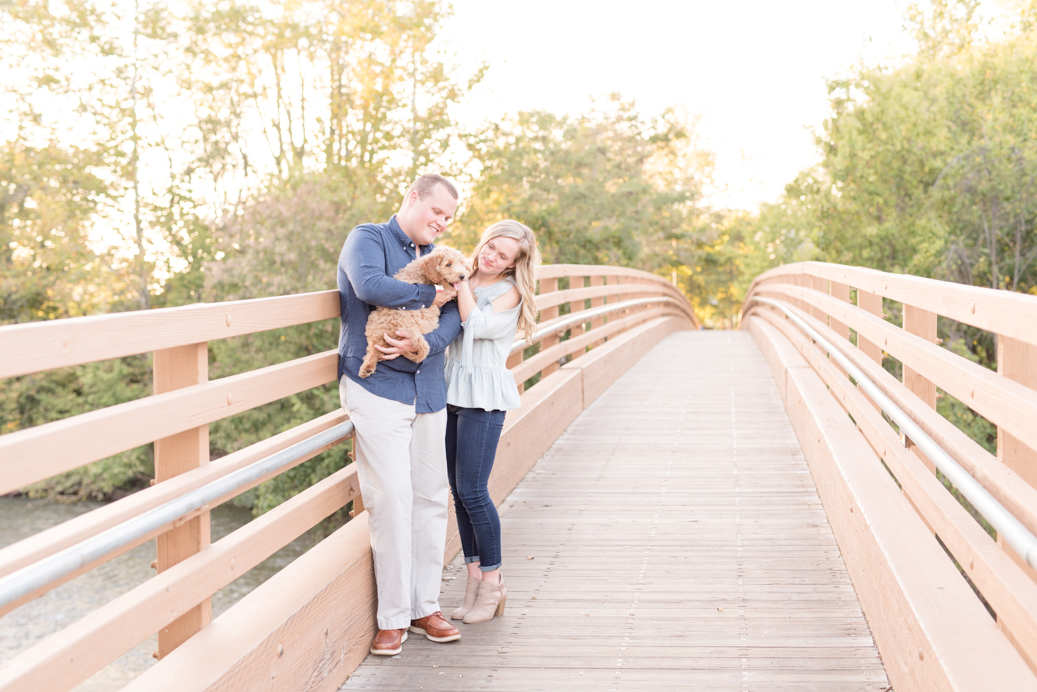 Couple looks at puppy while holding him on bridge.