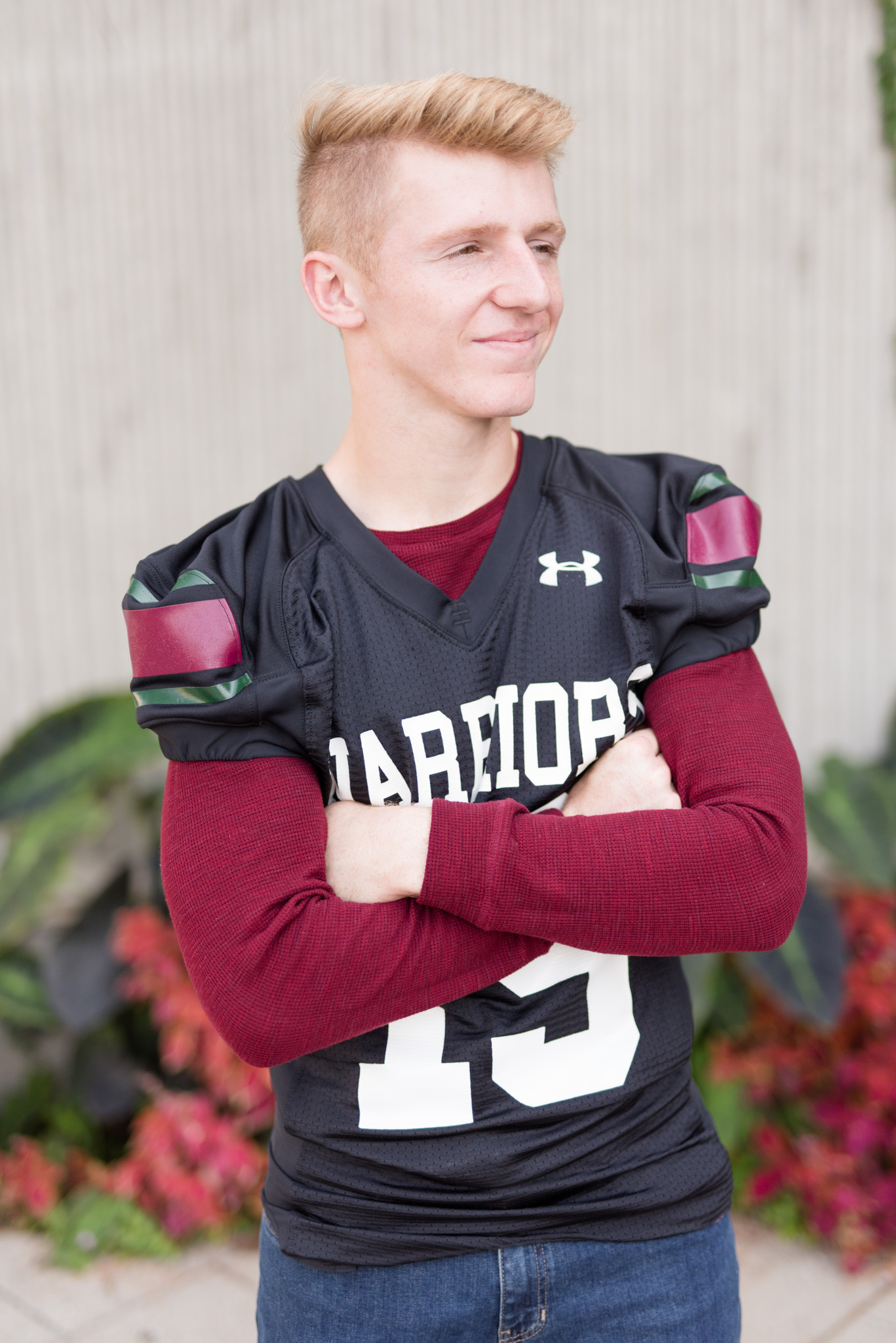 Senior guy looks off camera and crosses arms in football jersey.