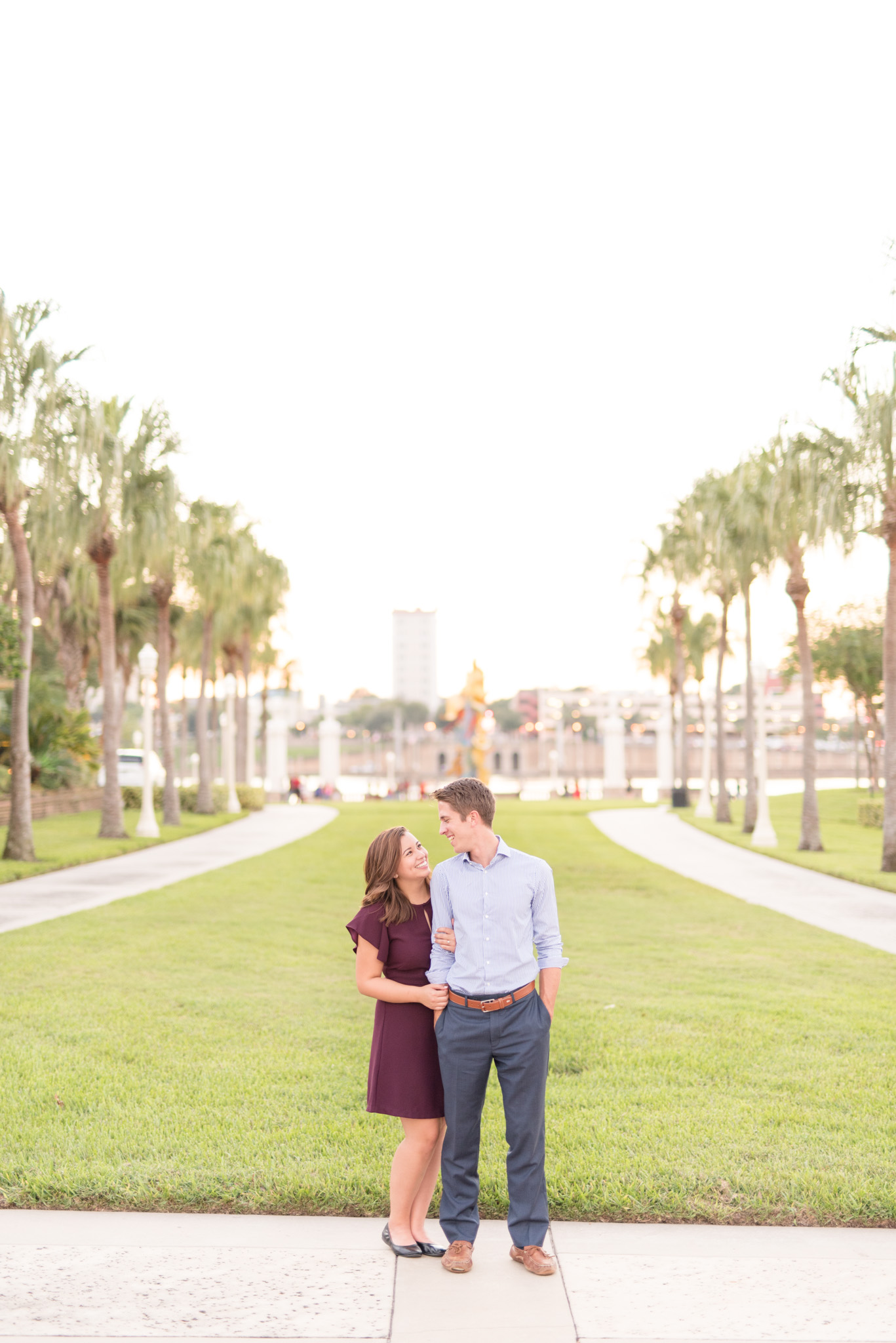 Engaged couple stands on palm tree path.