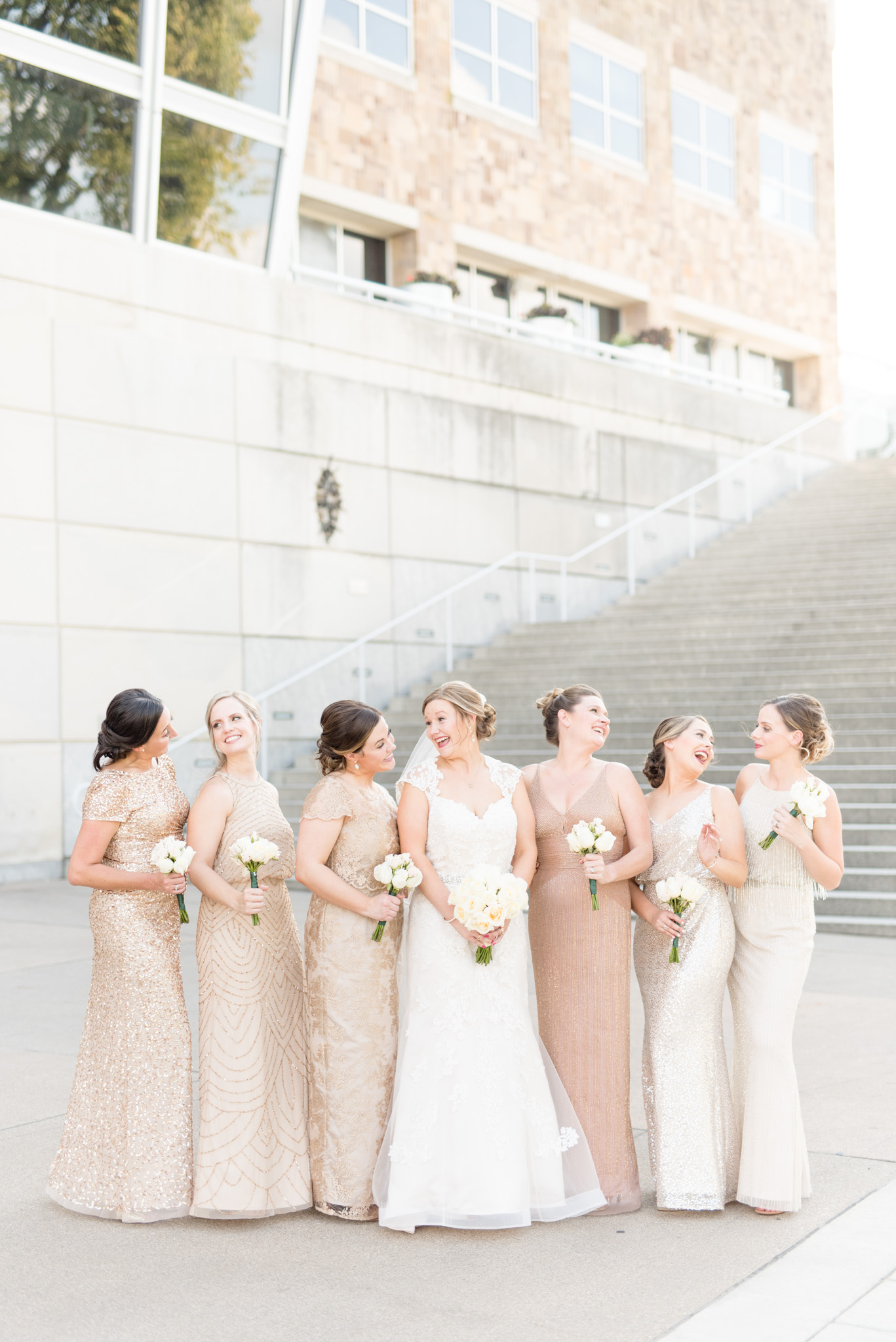 Bride and bridesmaids smile at each other downtown.