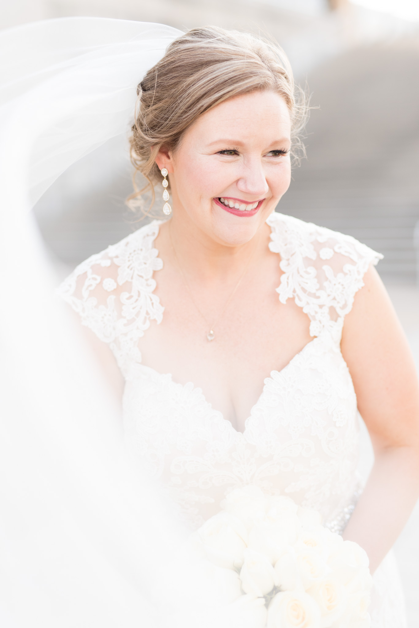 Bride looks to the side and laughs while veil blows.