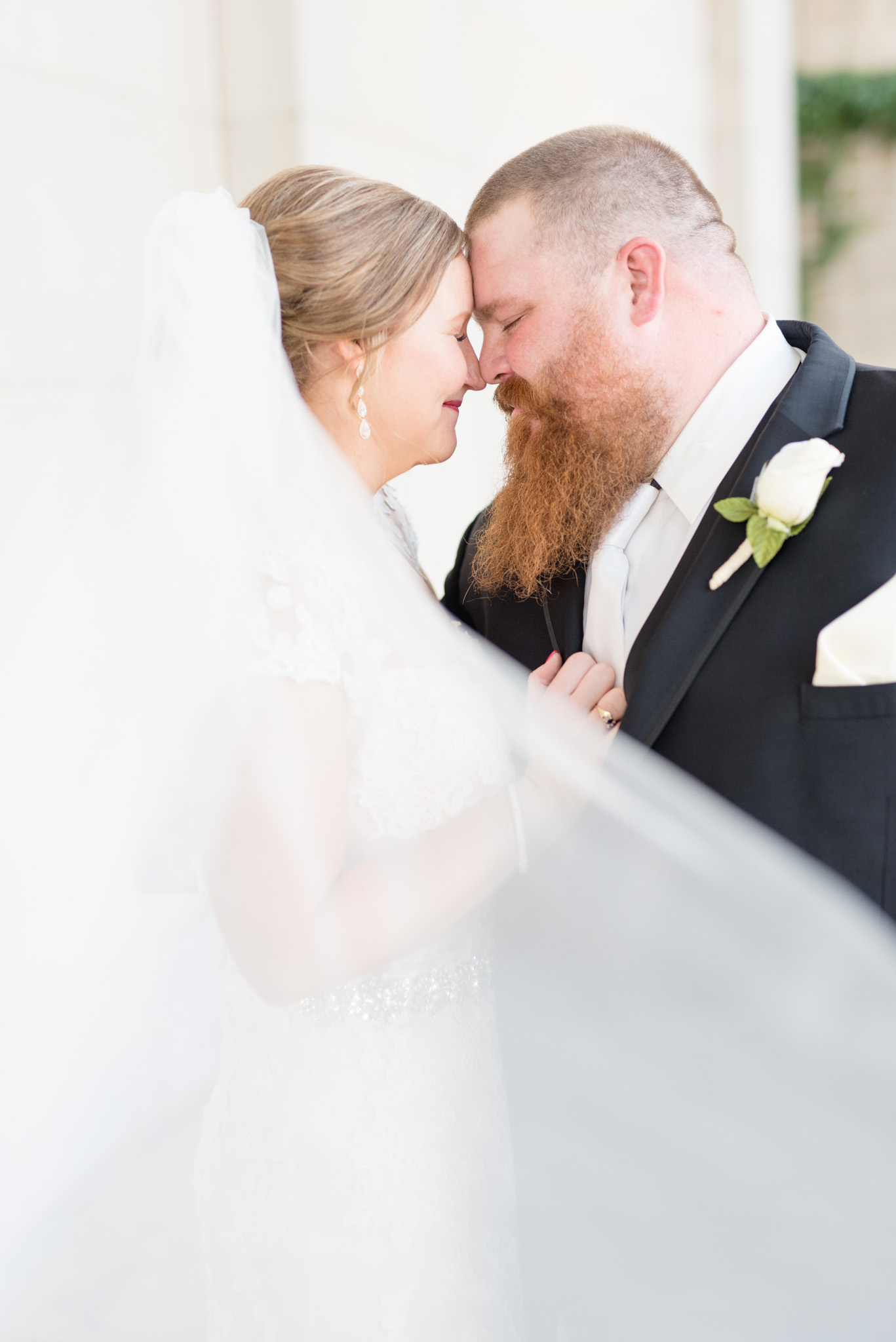 Bride and groom touch foreheads while veil blows.