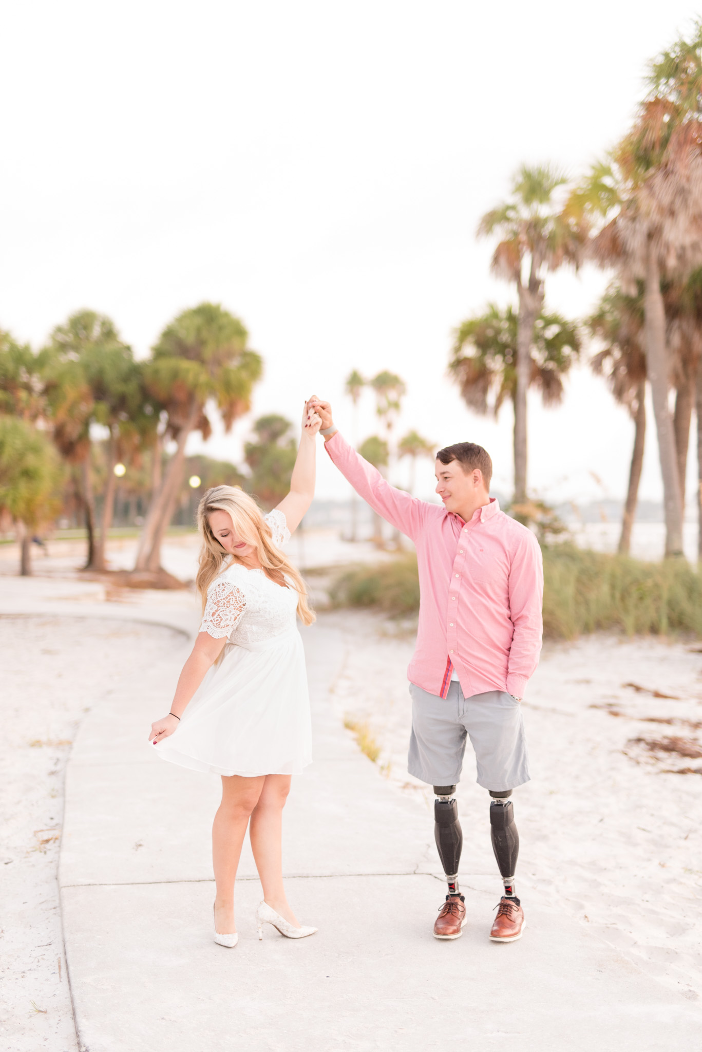 Groom twirls bride on sidewalk by beach.