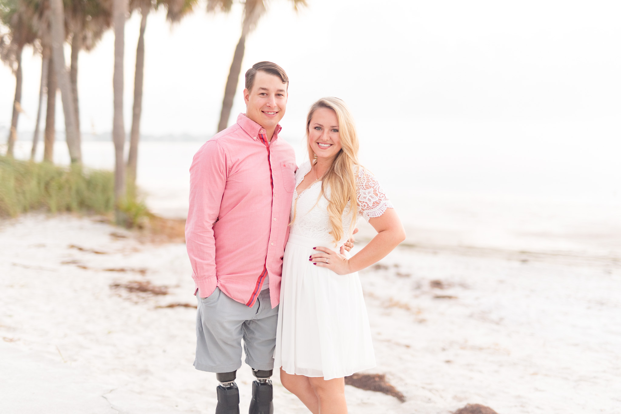 Couple smiles at camera while standing on beach.