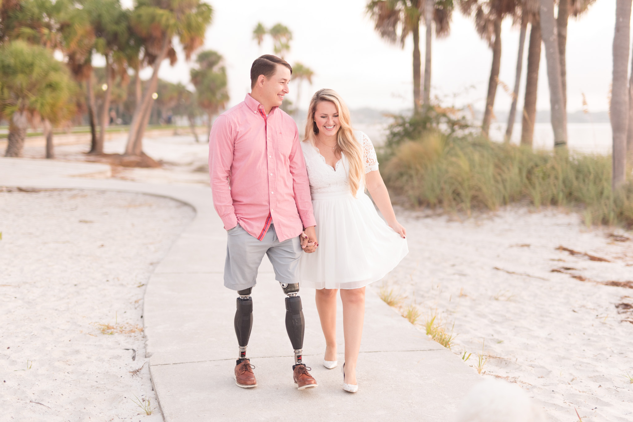 Couple walks down beach path and laughs.