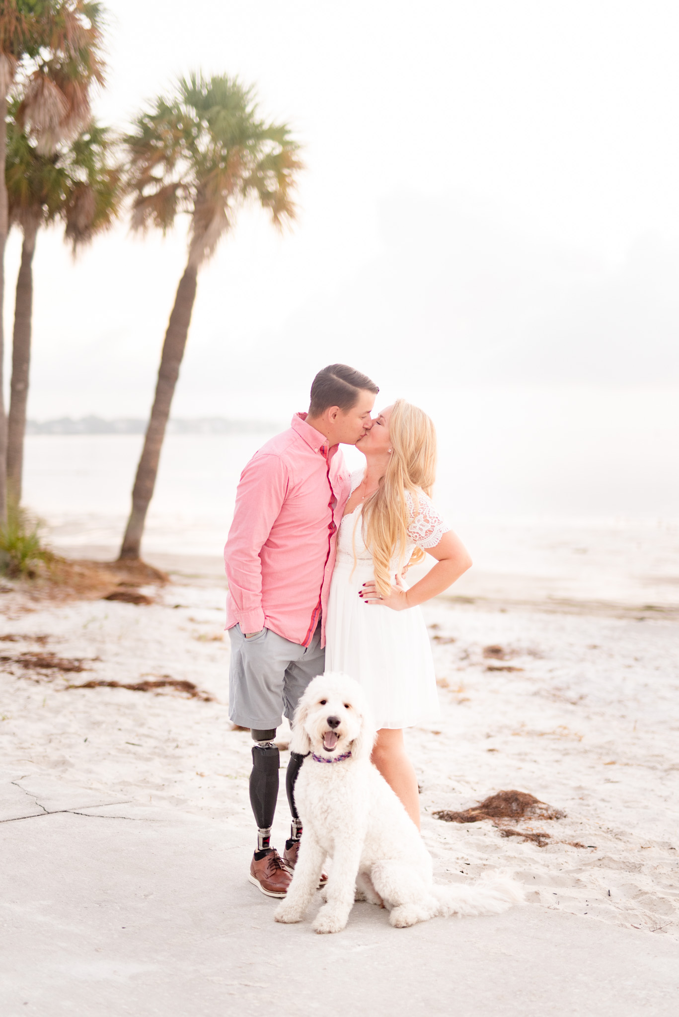 Couple kisses with goldendoodle.
