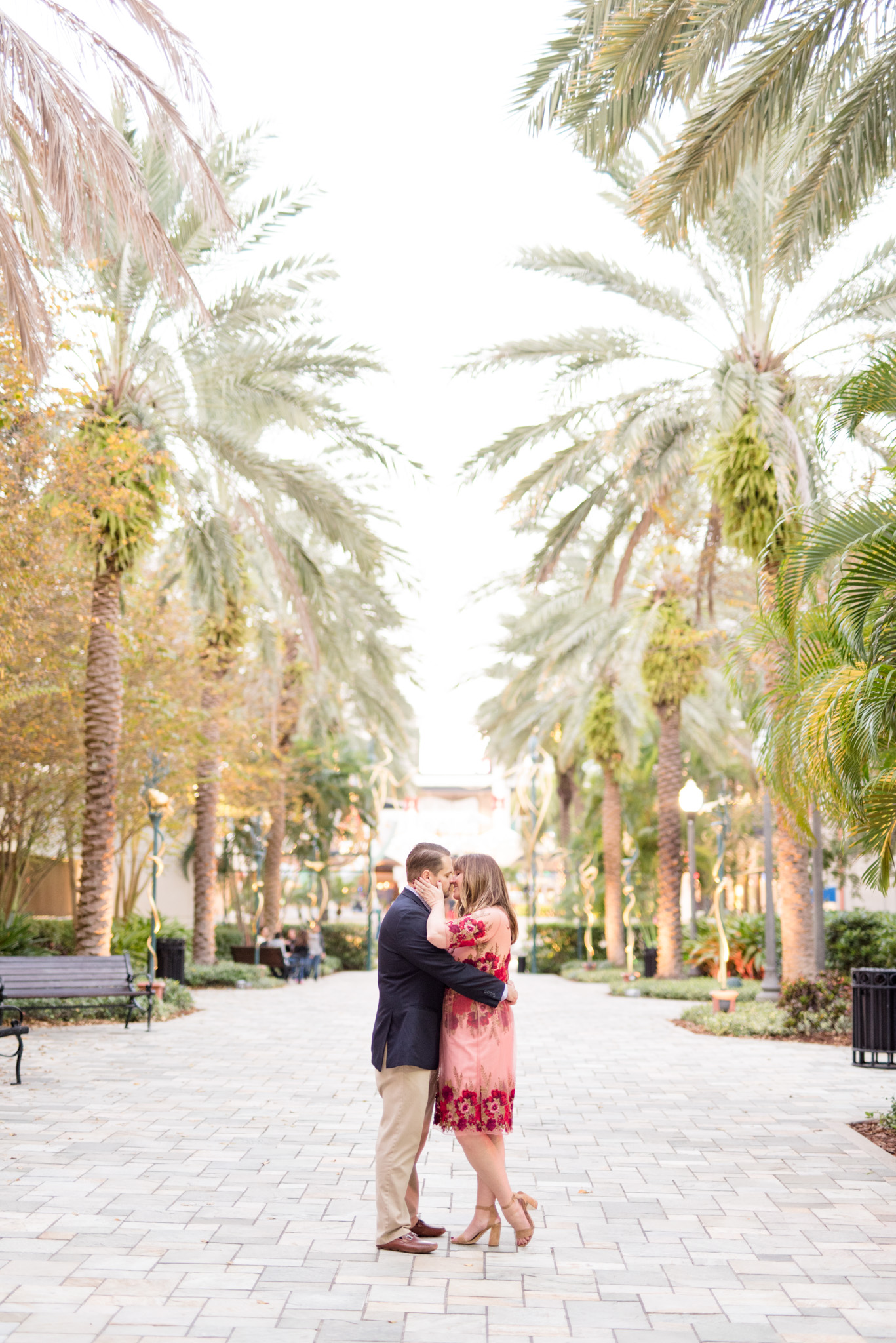 Couple kisses on palm tree lined path.