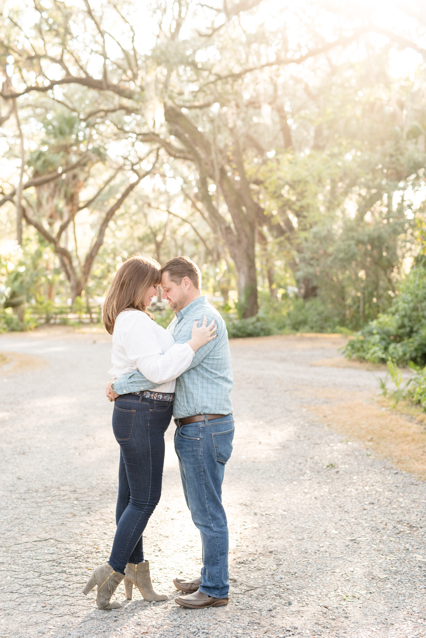 Couple cuddles under large oak trees.