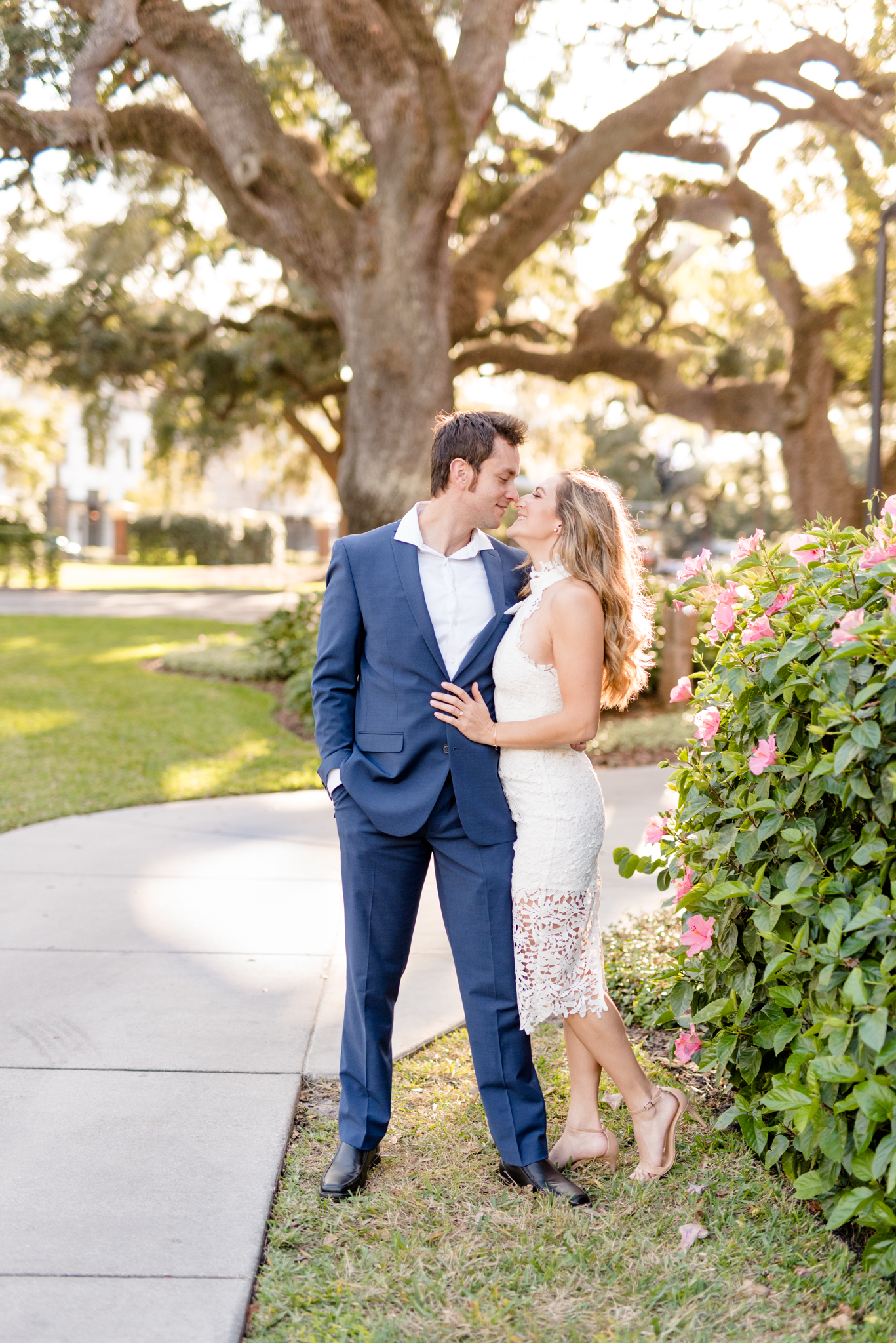 Couple leans in for kiss near oak trees.