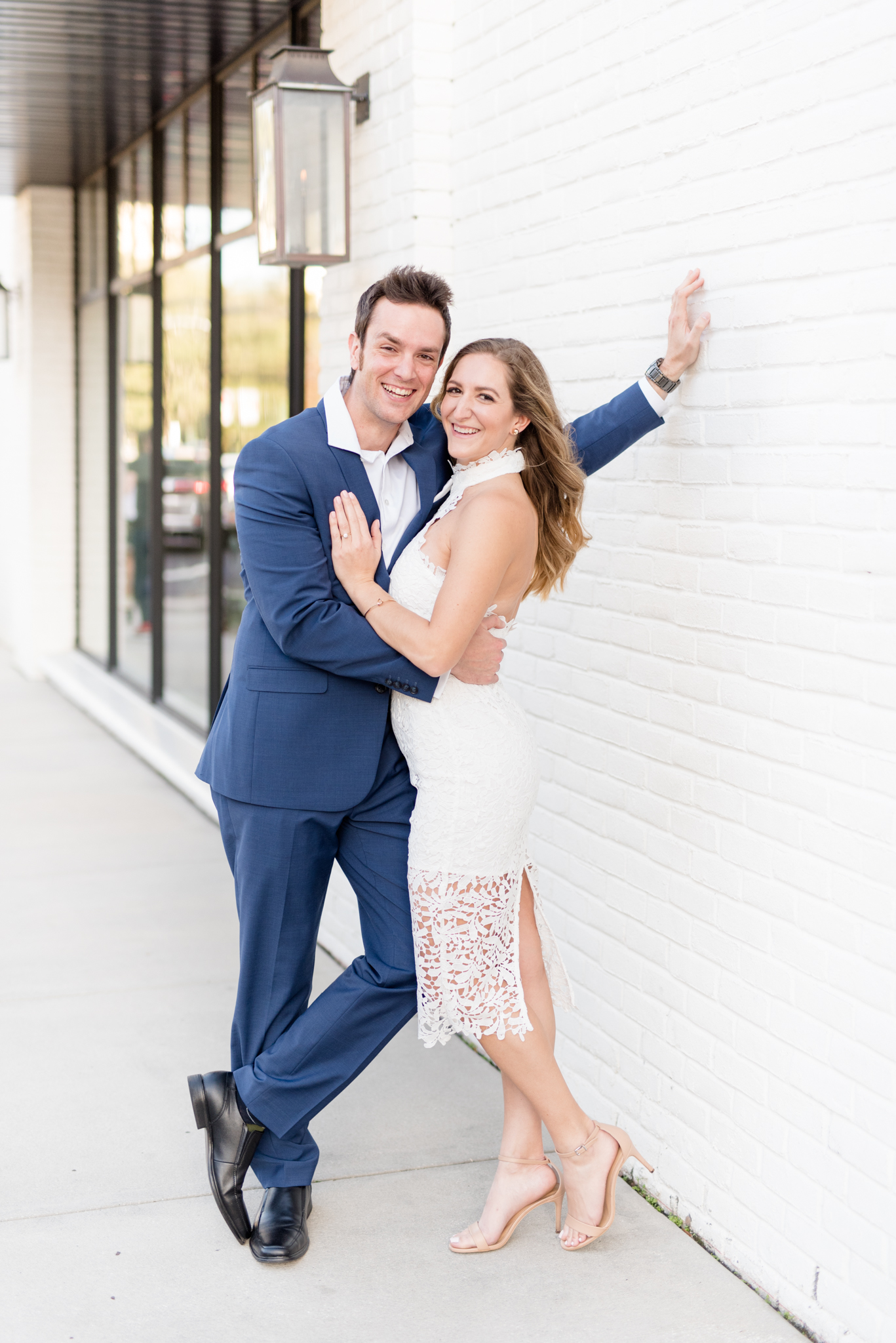 Couple laughs together near white wall.