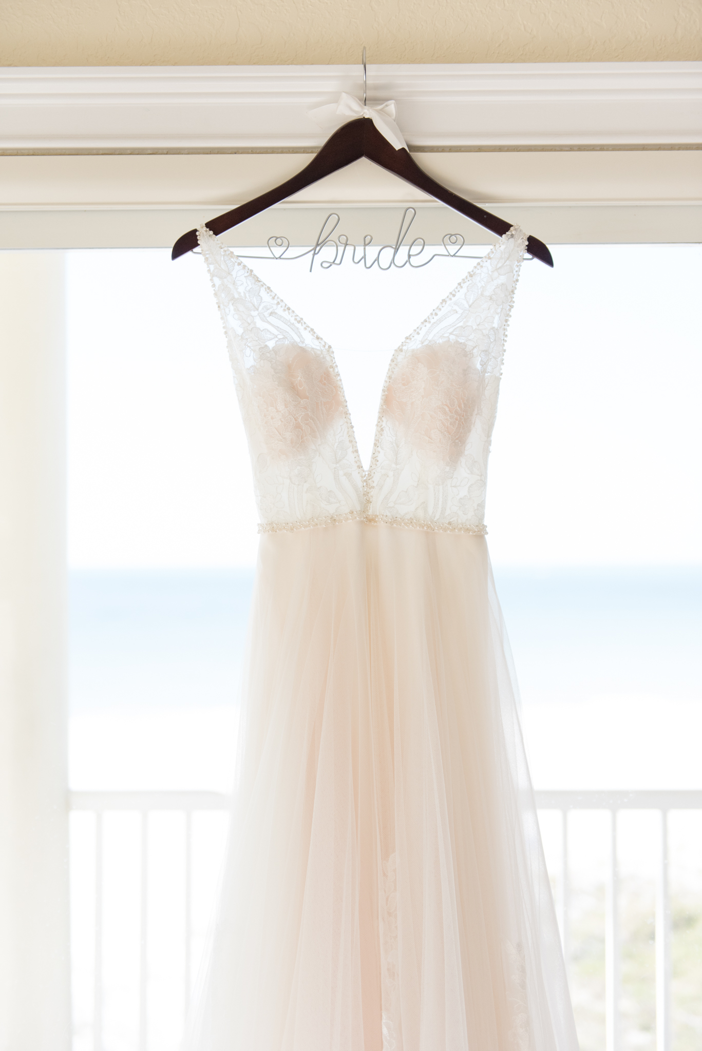 Wedding dress hangs in window.