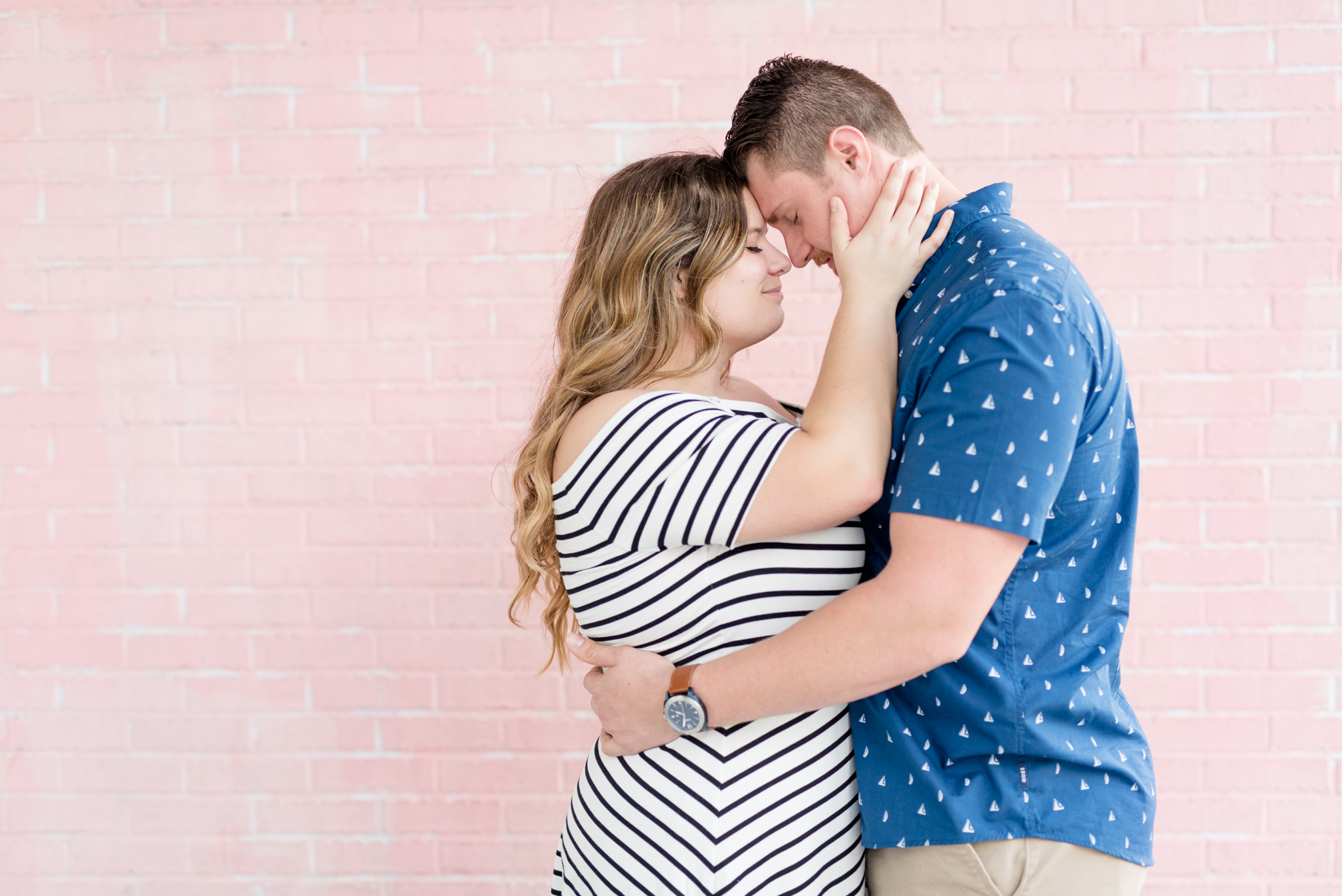 Couple snuggles in front of pink wall.