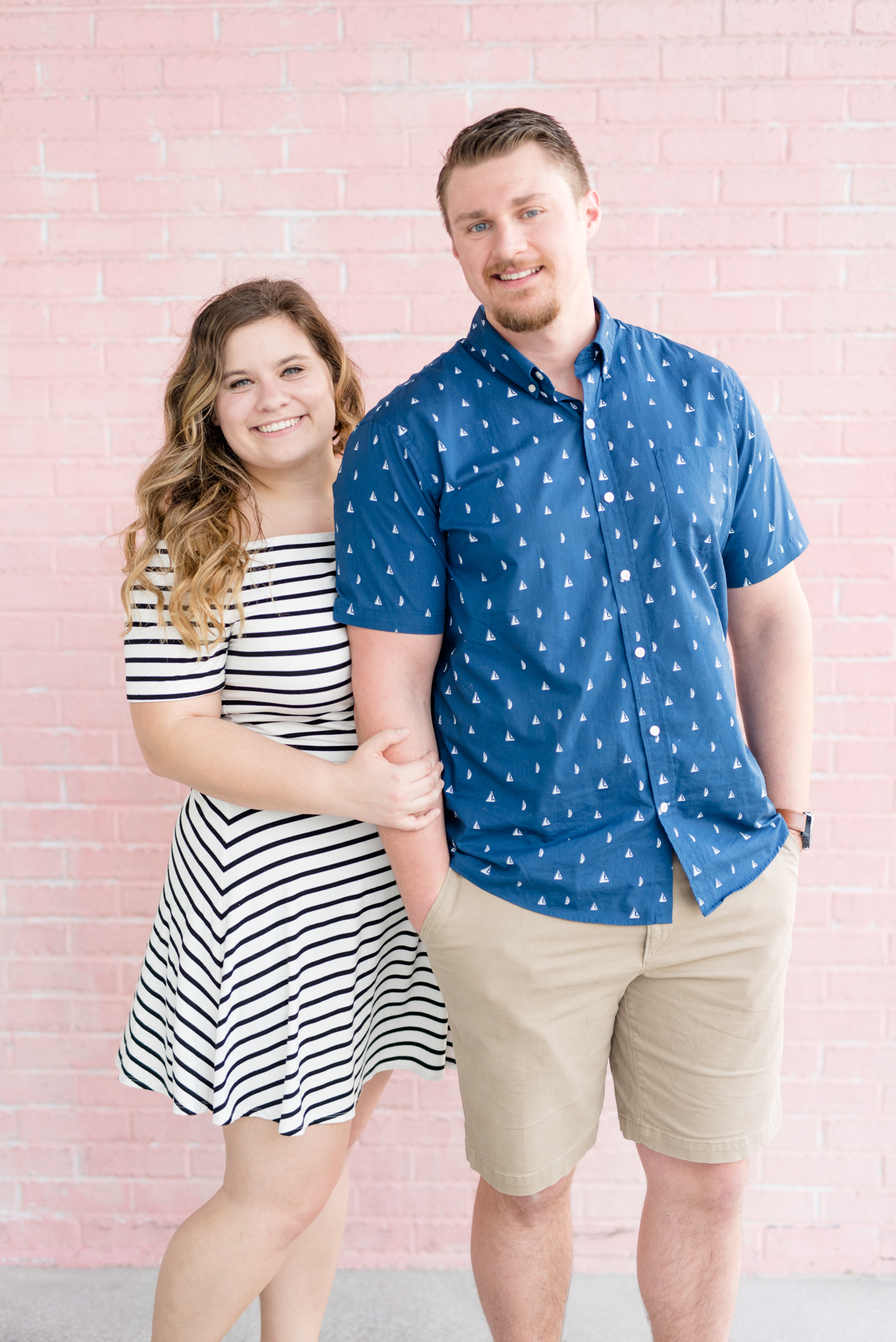 Couple smiles in front of pink wall.